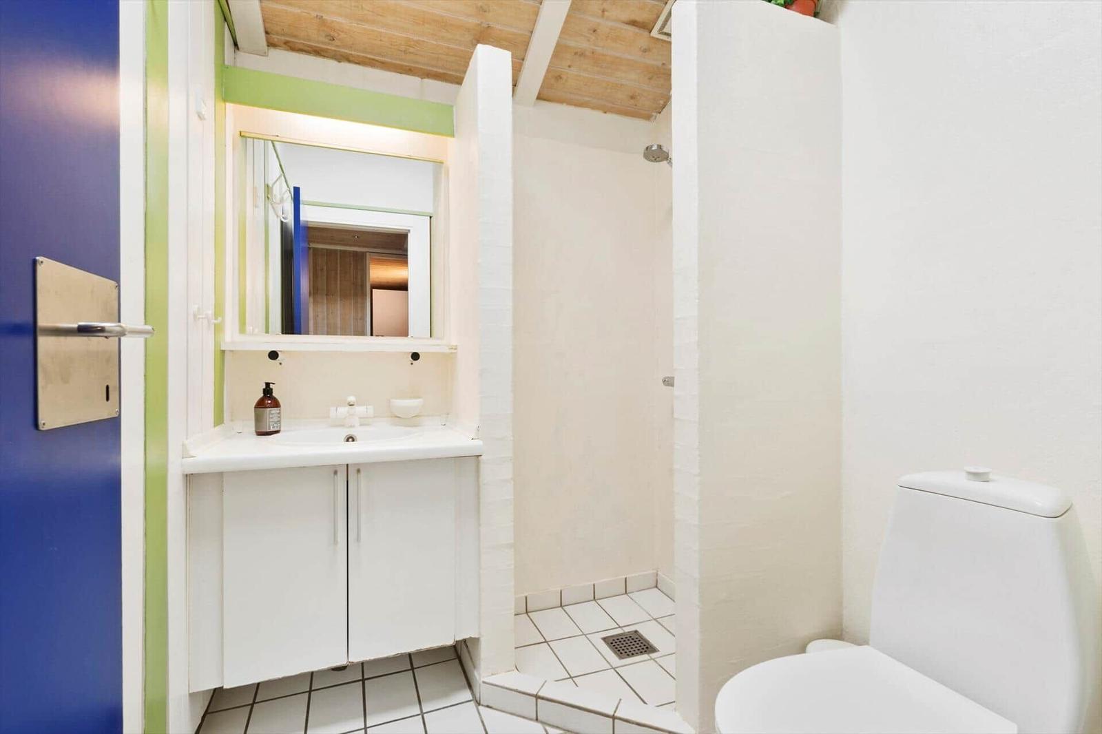 Bathroom with shower, sink, and toilet. Wooden ceiling and white tiles.