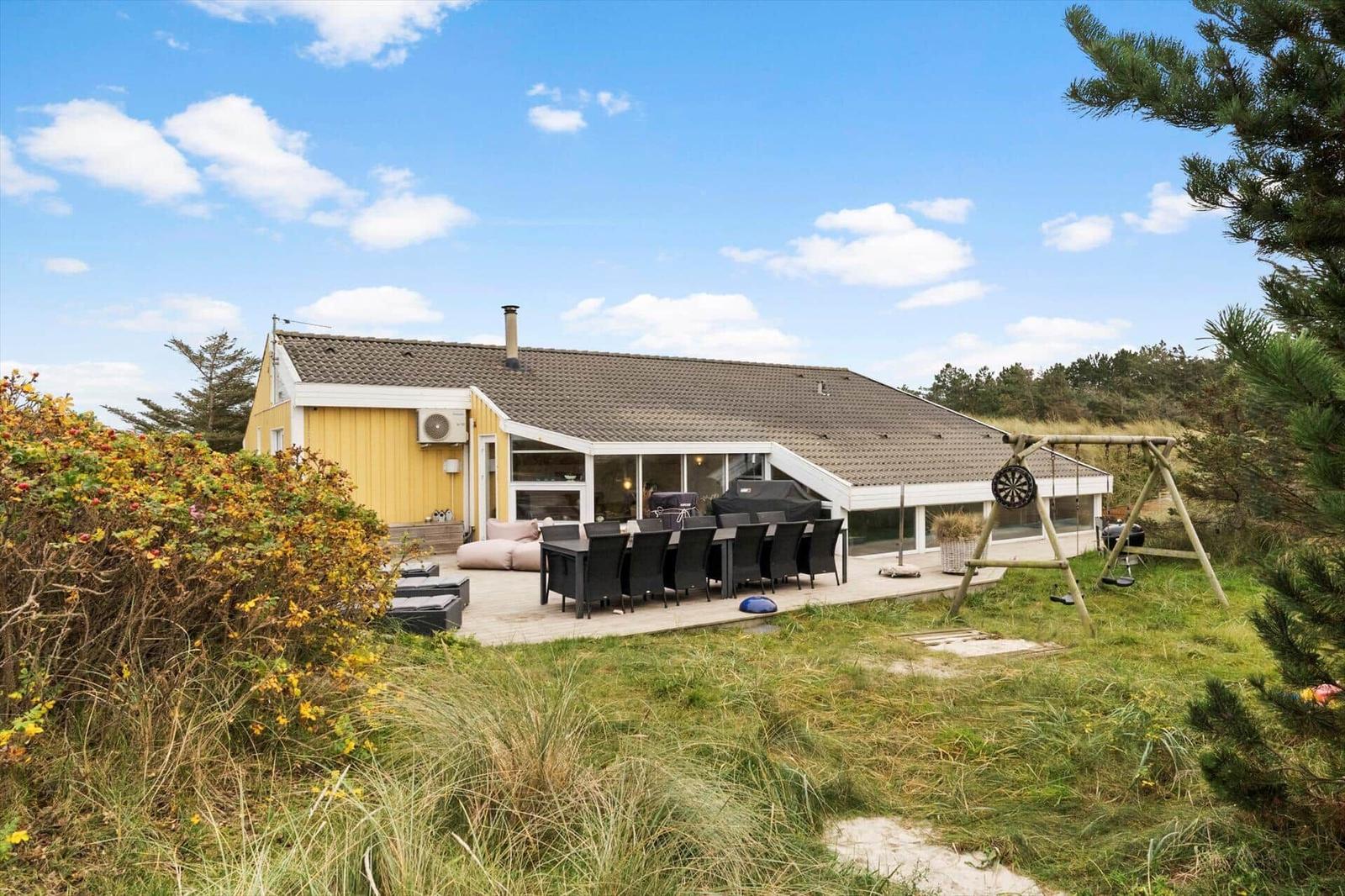 A yellow house with terrace, grill, and swing in the garden.