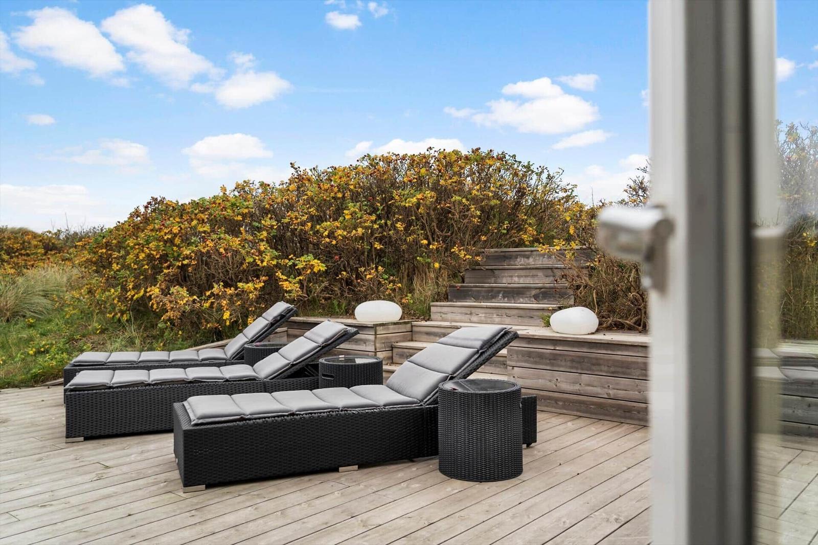 Deck with loungers and tables, view of hedges and steps.