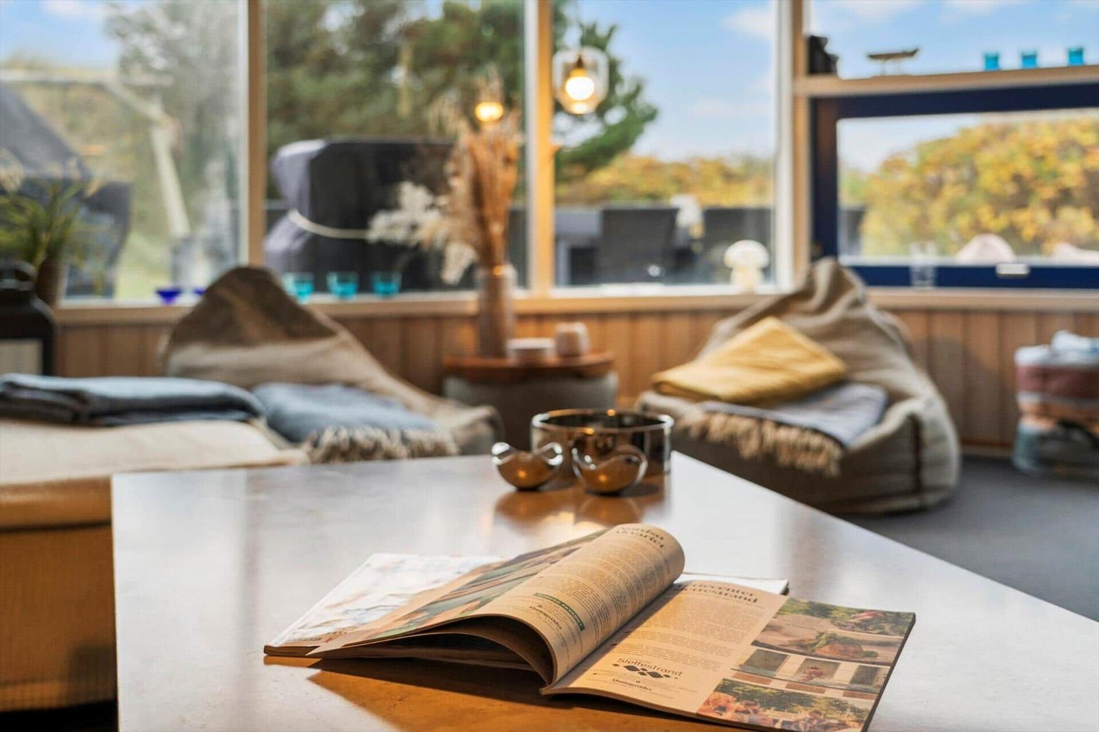 A table with an open magazine. In the background are two seats and large windows.