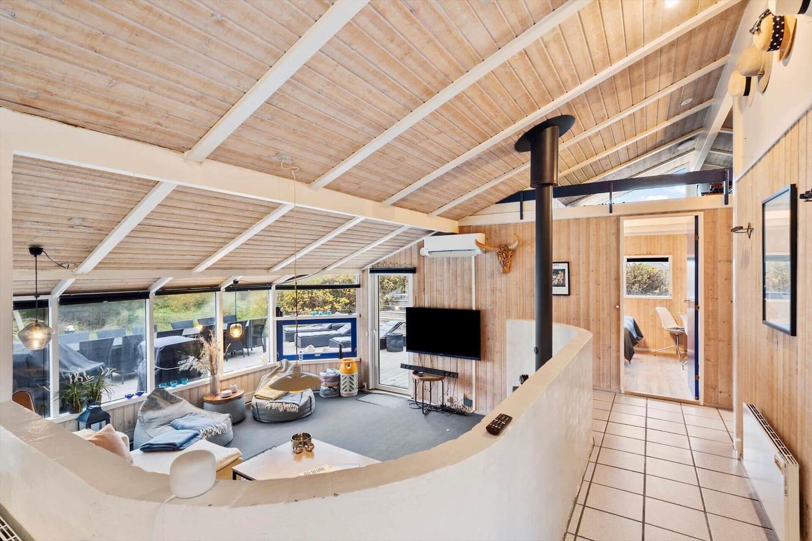 Living area with wooden ceiling, TV, and view of terrace.