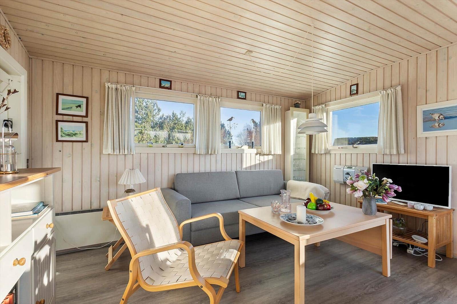 Wohnzimmer mit Sofa, Sessel und Tisch. Fenster mit Blick auf Wald.