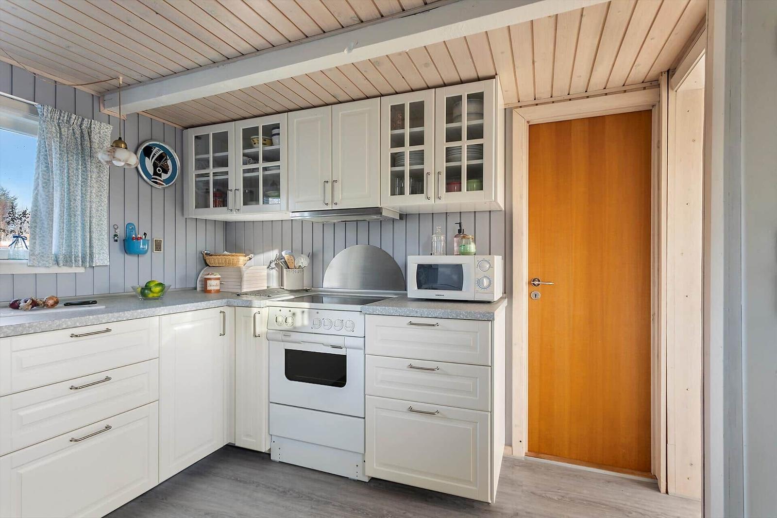 Küche mit weißen Schränken, Herd und Mikrowelle. Holzwand und Tür sichtbar.