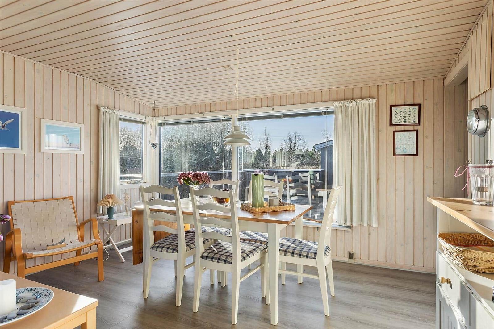 Esszimmer mit Tisch, Stühlen und großem Fenster. Holzwände und Boden.