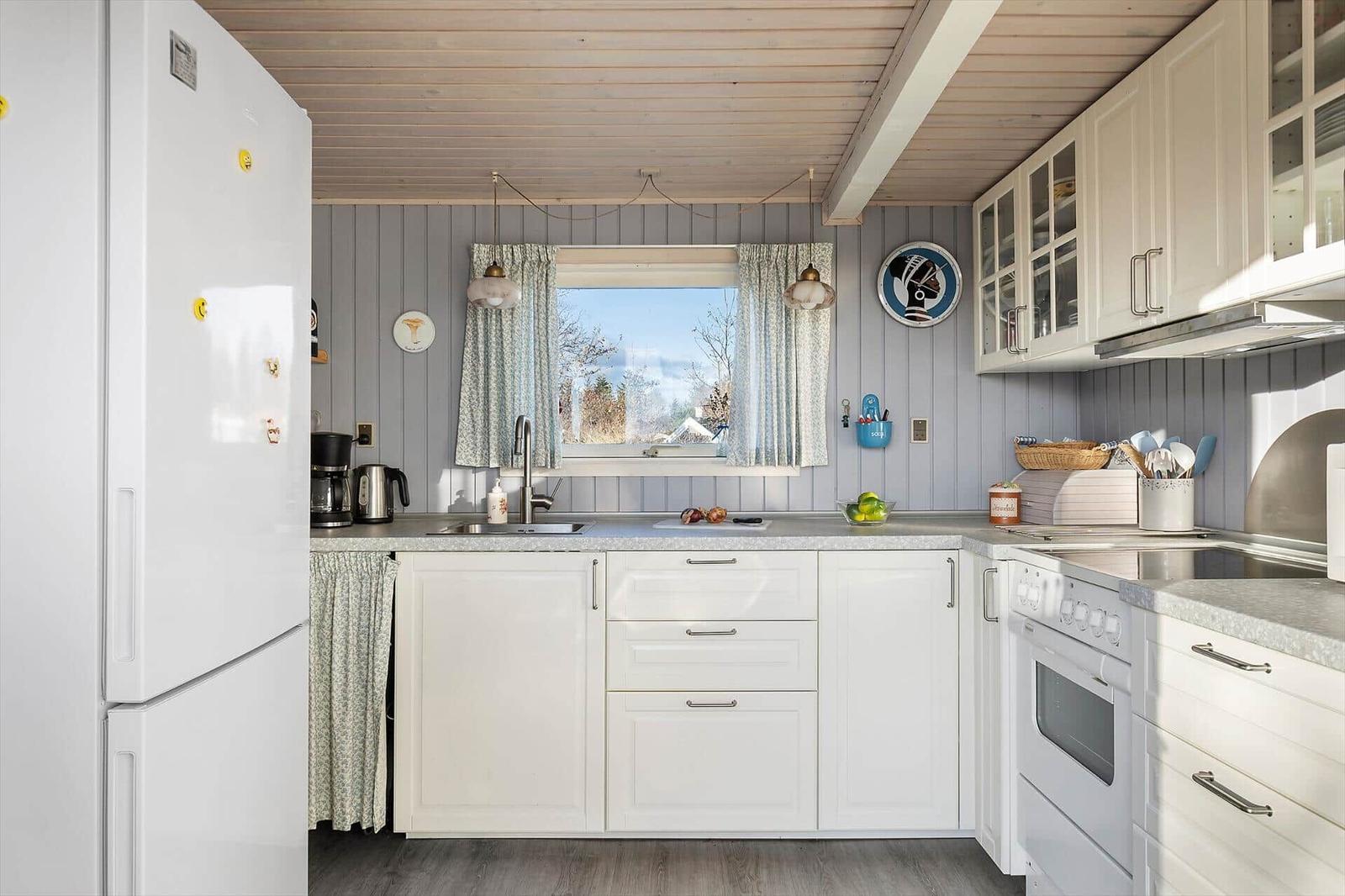 Küche mit weißer Einbauküche, Kühlschrank und Fenster mit Blick nach draußen.
