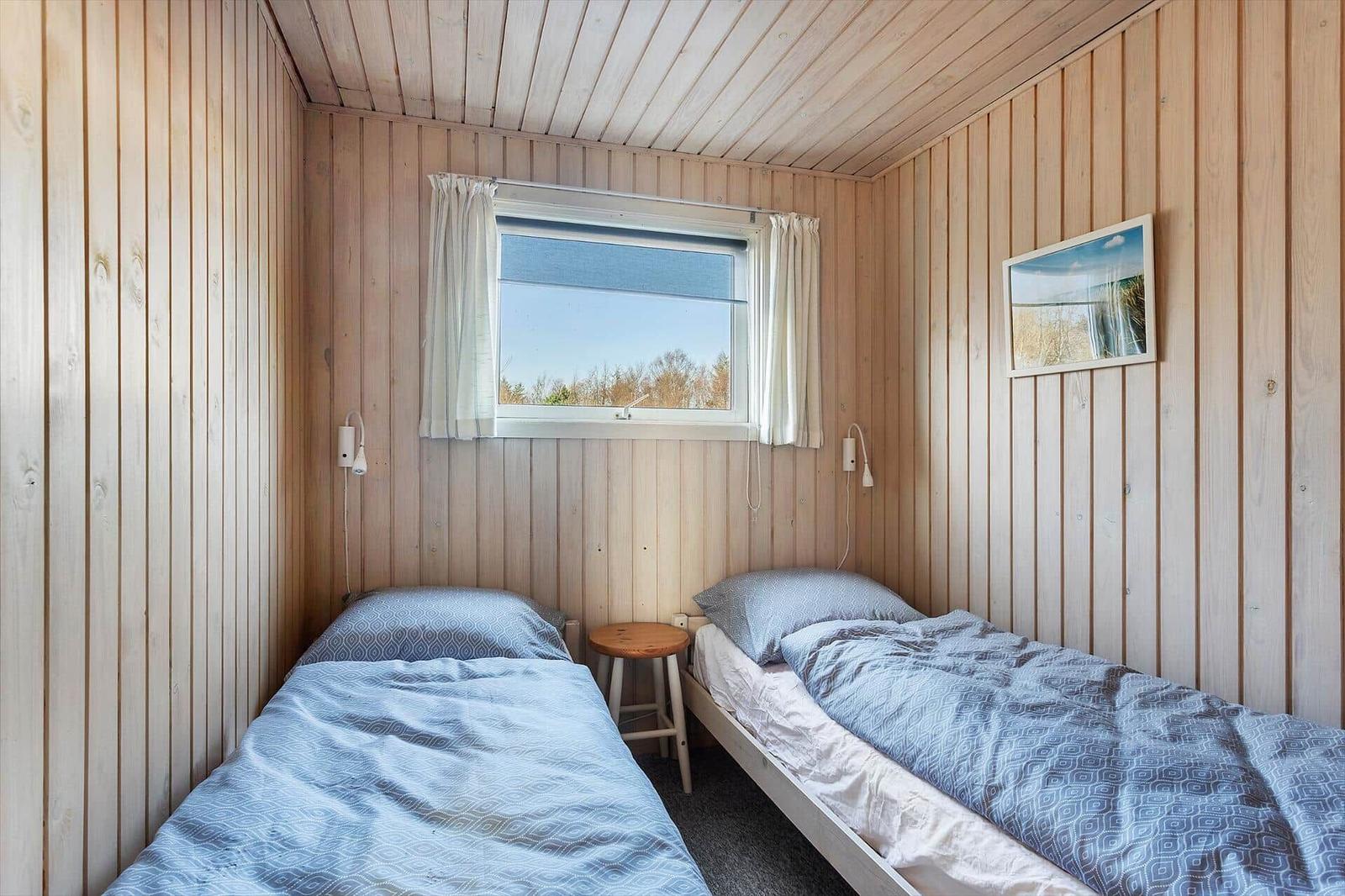 Zwei Einzelbetten in einem holzverkleideten Raum mit Fenster und Bild.