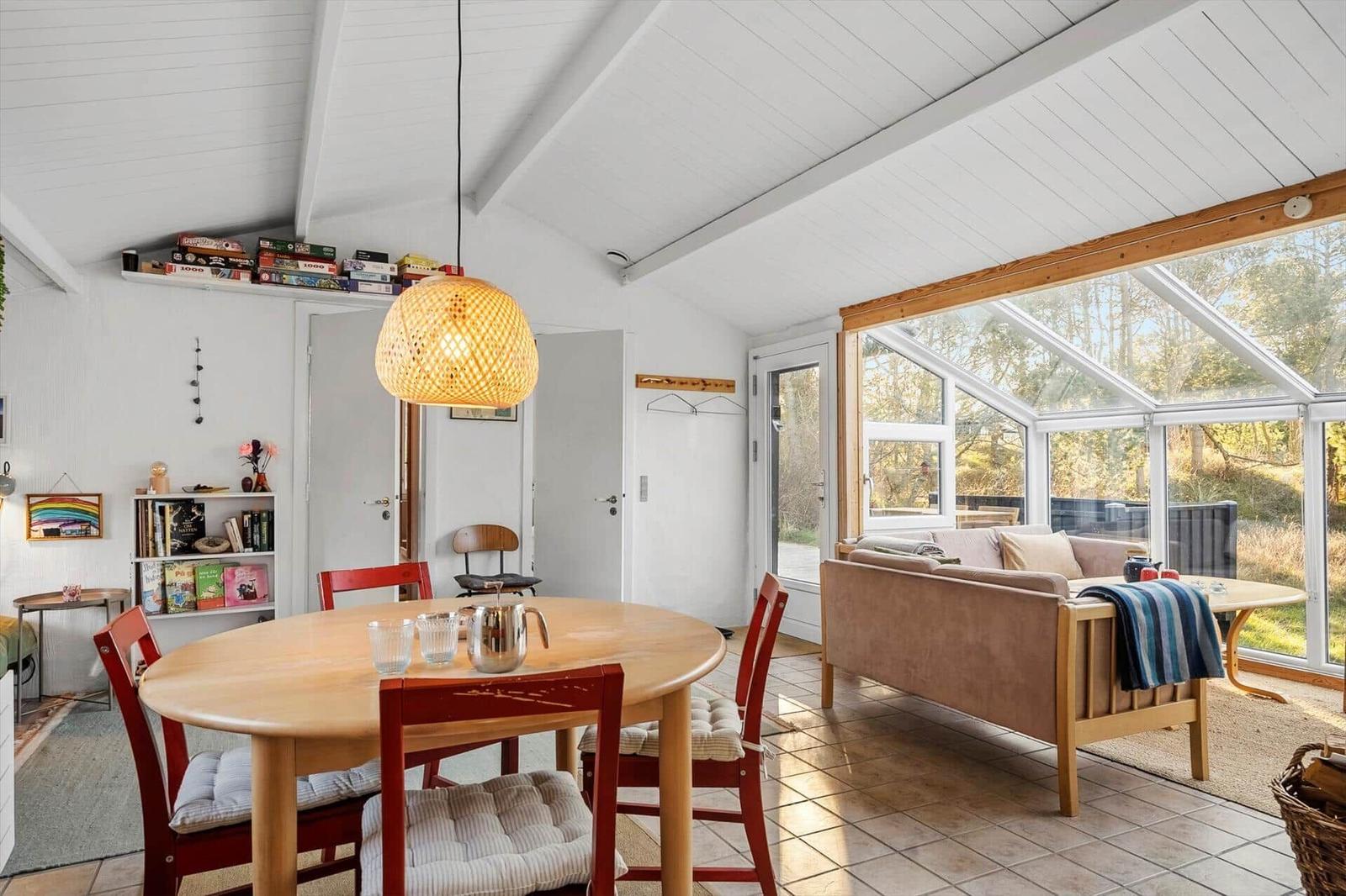 Essbereich mit runden Tisch und roten Stühlen. Wohnbereich mit Sofa und Glasfront.