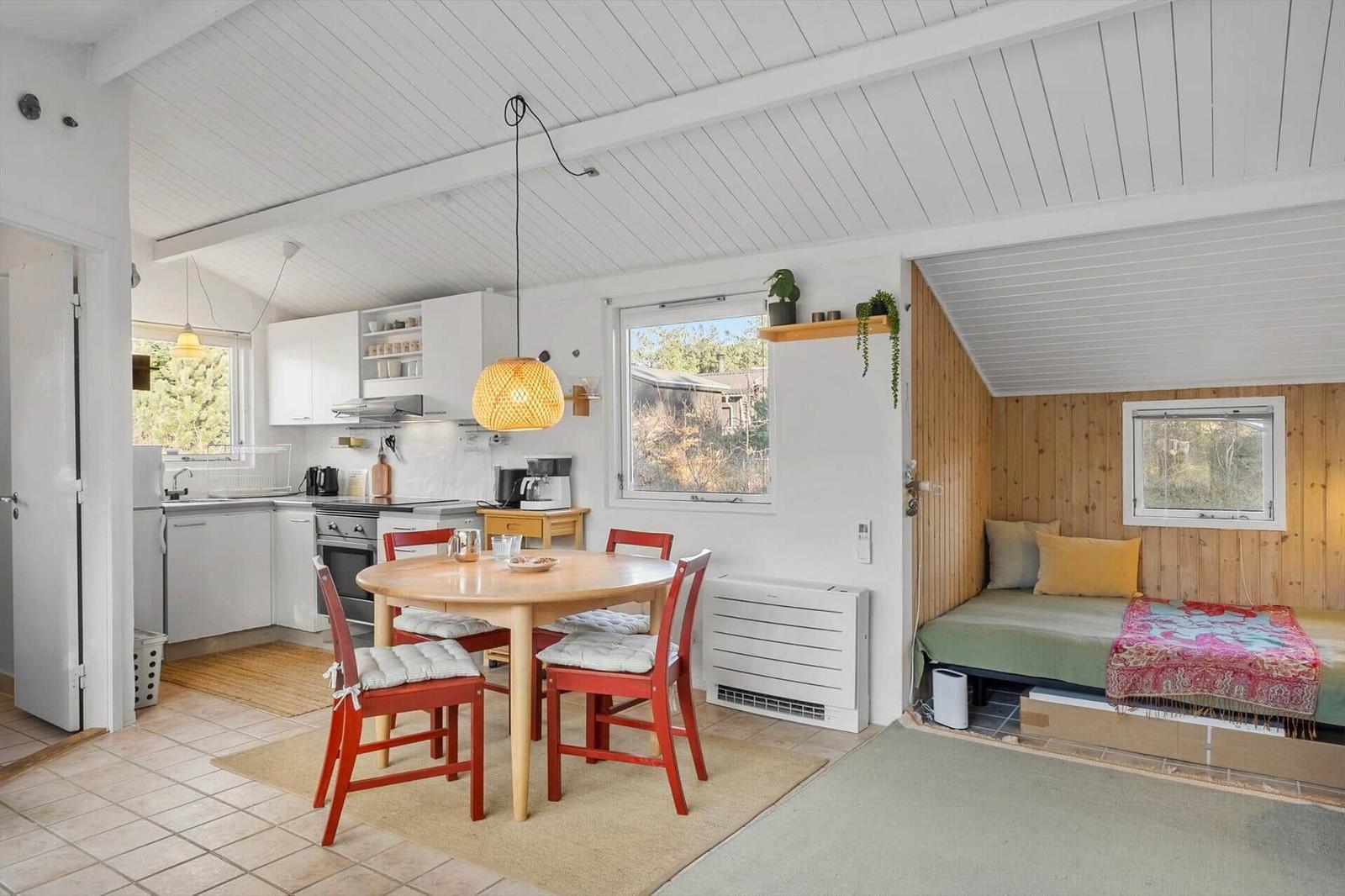 Küche, Essbereich und Schlafbereich in einem Ferienhaus mit Holzwänden und weißen Decken.