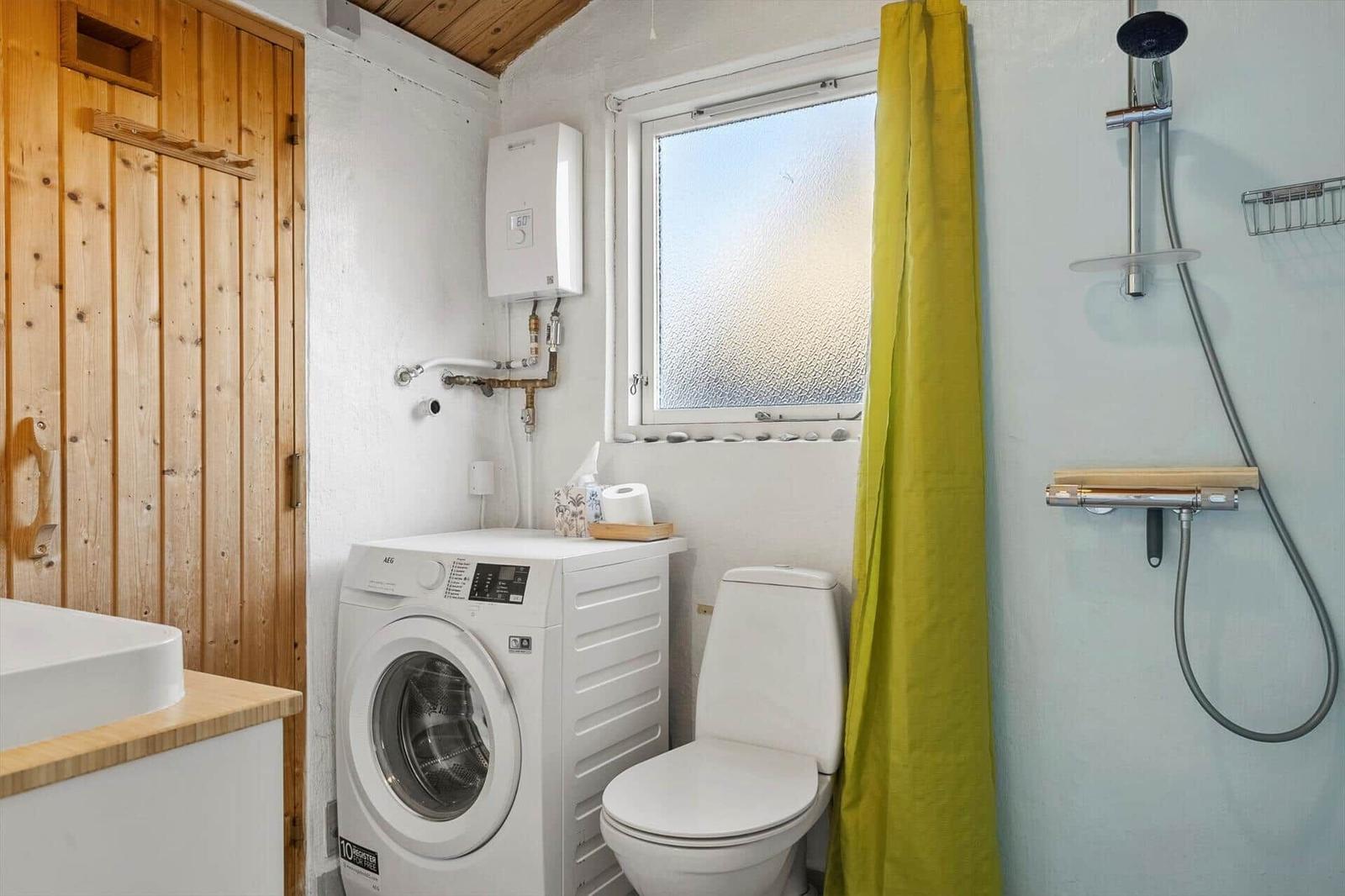Badezimmer mit Dusche, Toilette und Waschmaschine. Holztür und Fenster mit Steinverkleidung.