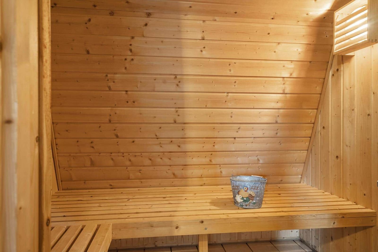 Sauna mit Holzwand und Sitzbank. Auf der Bank steht ein Metalleimer.
