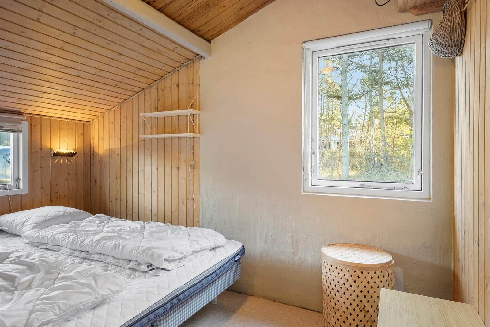 Schlafzimmer mit Bett, Fenster und Holzwand