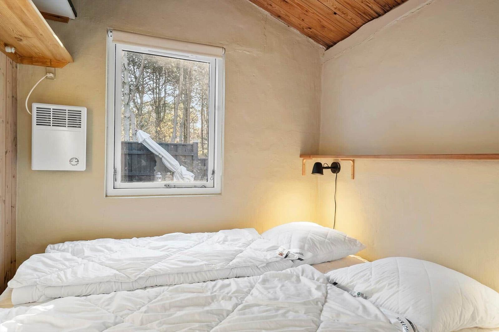 Schlafzimmer mit Bett, Fenster und Wandheizung.