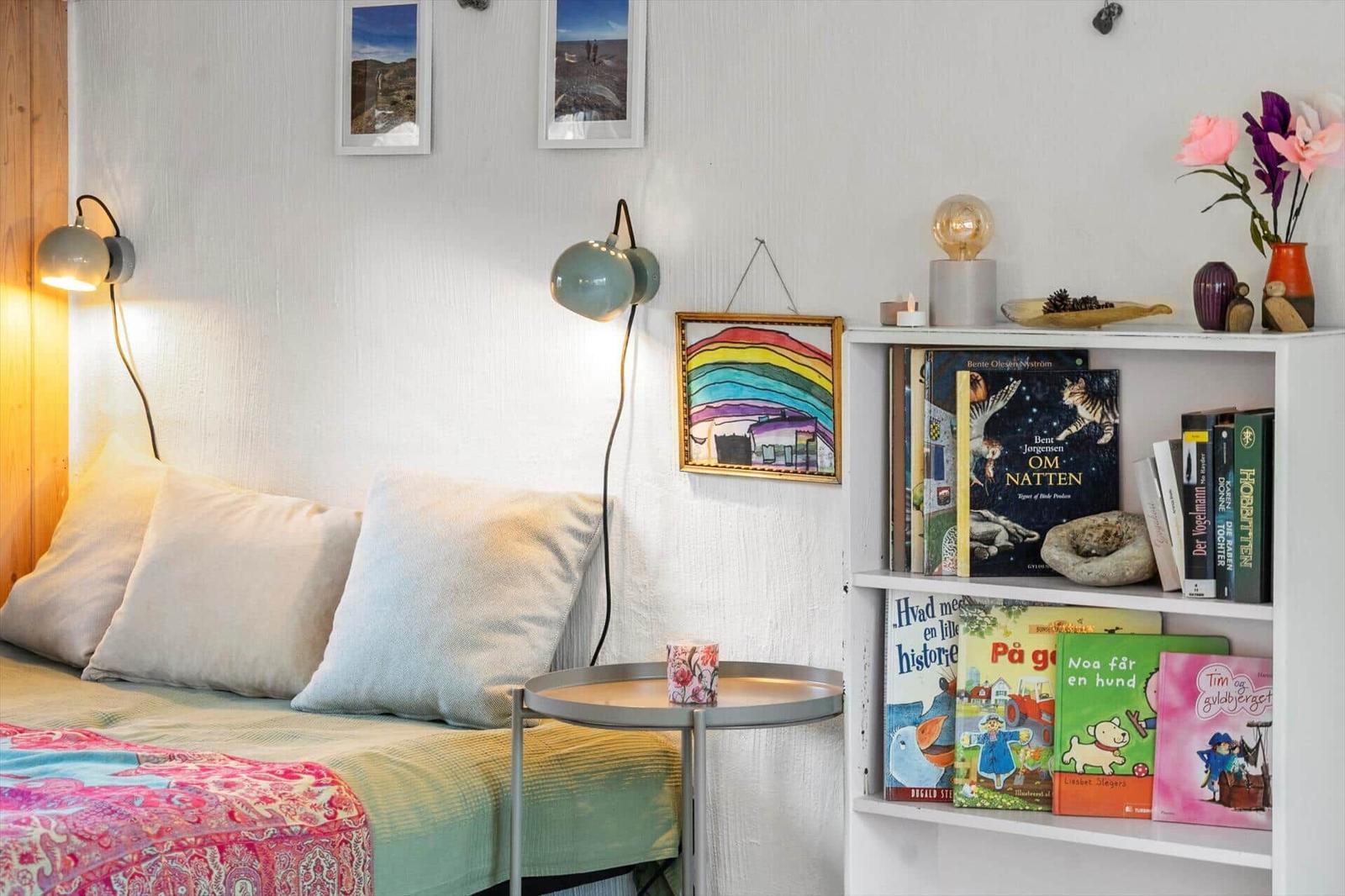 Schlafzimmer mit Bett, Nachttisch, Bücherregal und Wandlampen.