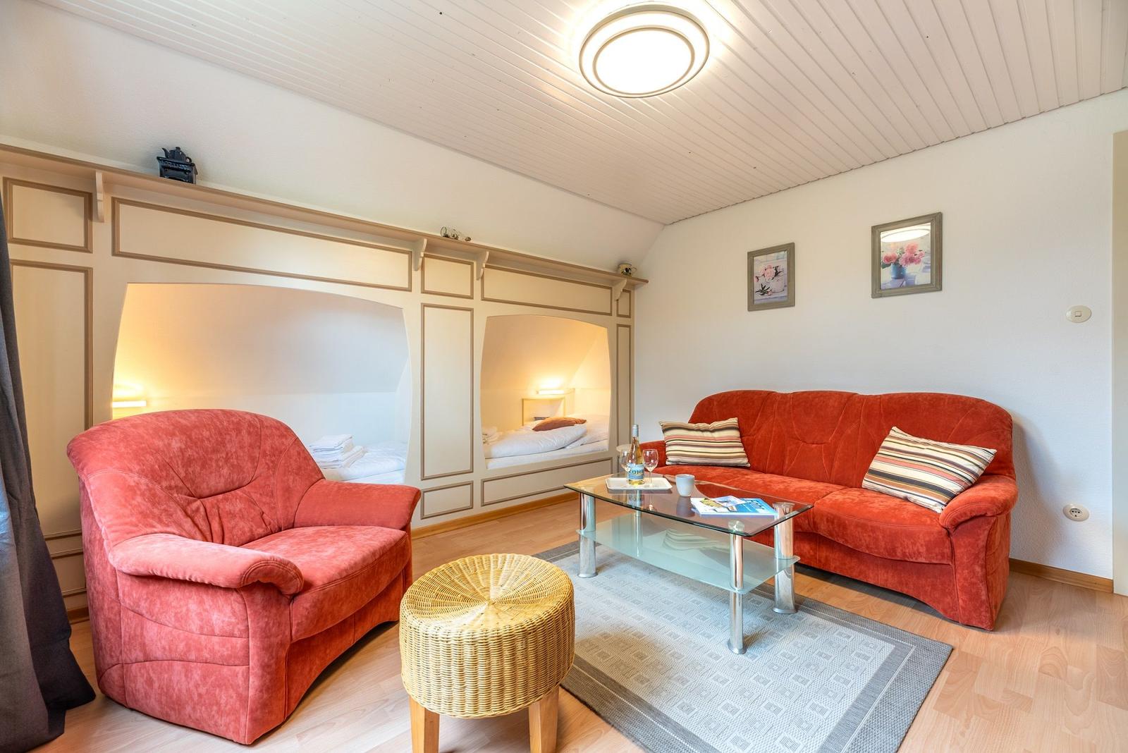 Wohnzimmer mit rotem Sofa und Sessel, Glas-Tisch und zwei Schlafnischen.