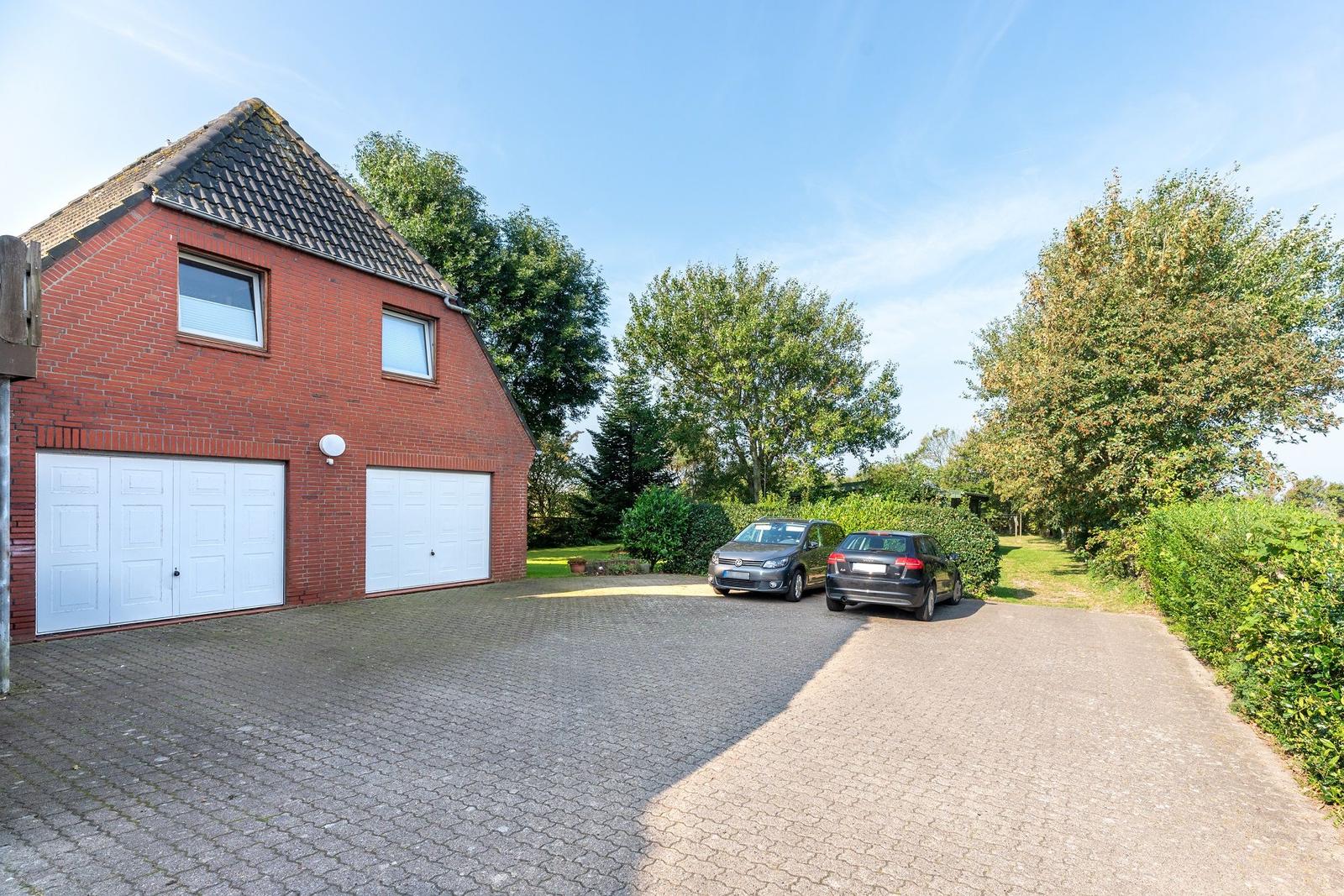 Rotes Backsteingebäude mit zwei Garagen und gepflastertem Vorplatz mit zwei Autos.