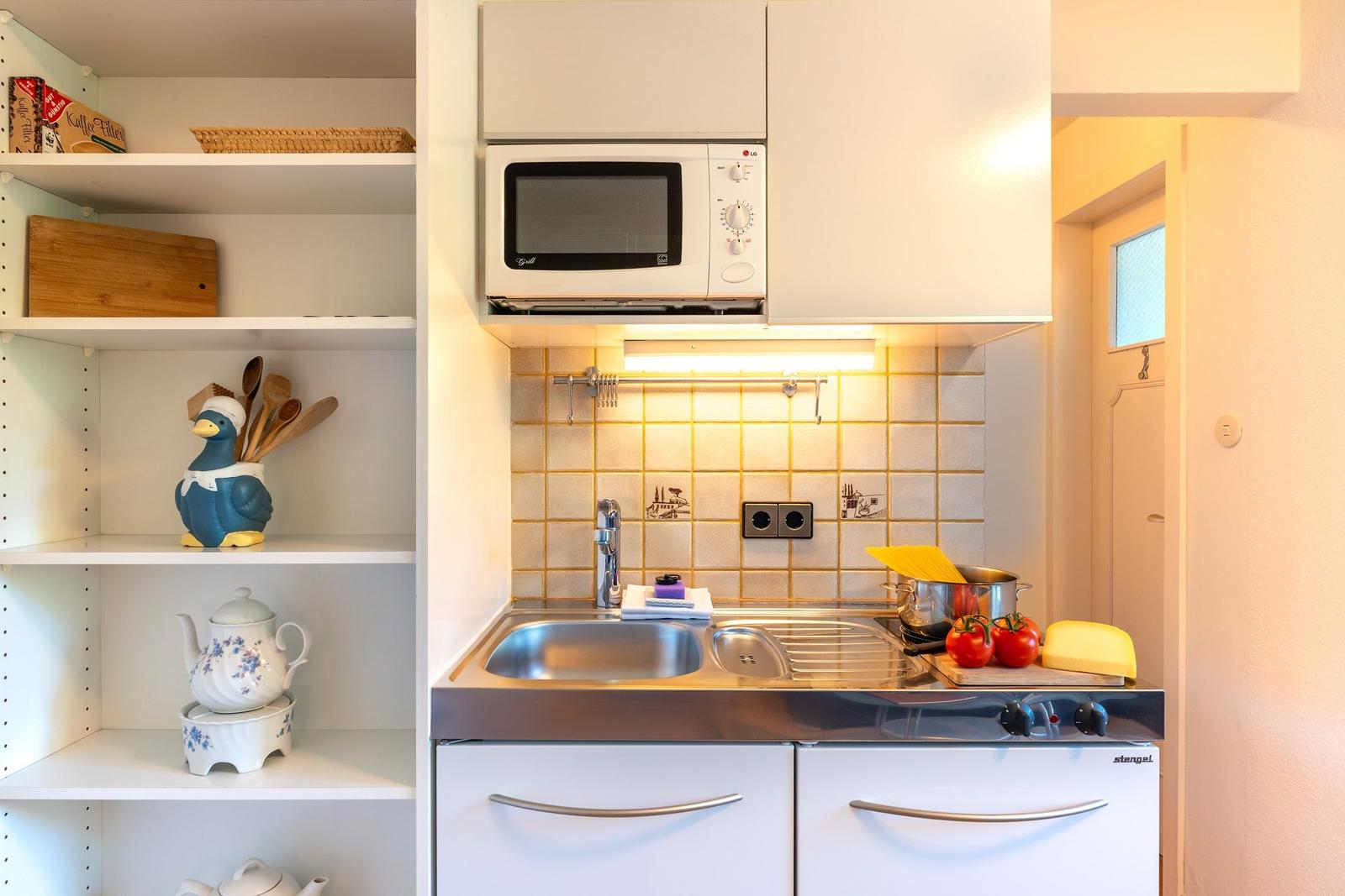 Küche mit Spüle, Herd und Mikrowelle. Regal mit Küchenutensilien und Kaffeefiltern.