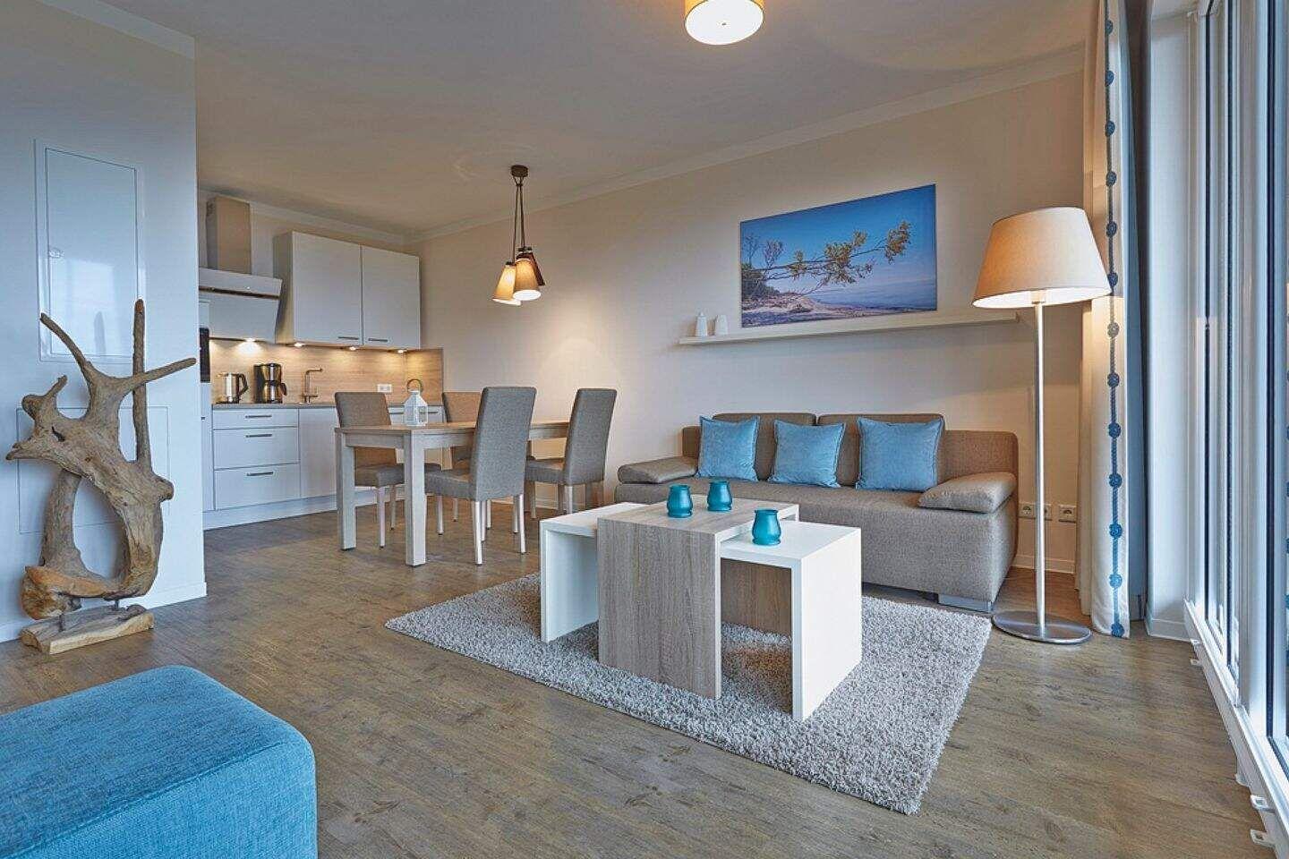 Wohn- und Essbereich mit Sofa, Tisch und Küchenzeile. Große Fenster und modern eingerichtet.