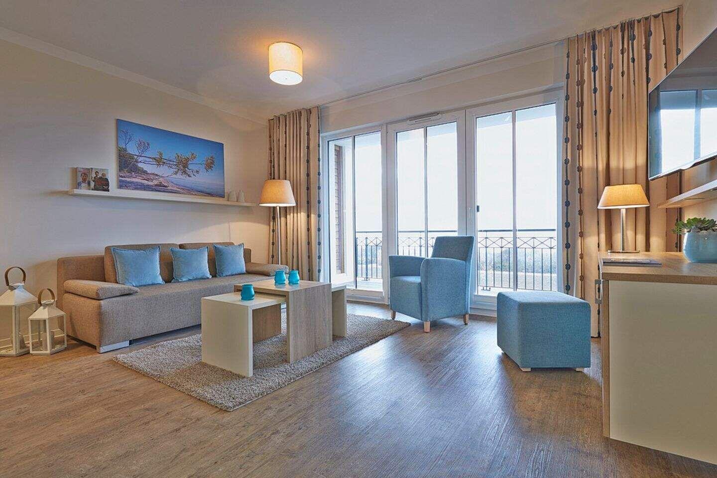 Wohnzimmer mit Sofa, Sessel und Terrasse. Holzboden und große Fenster.