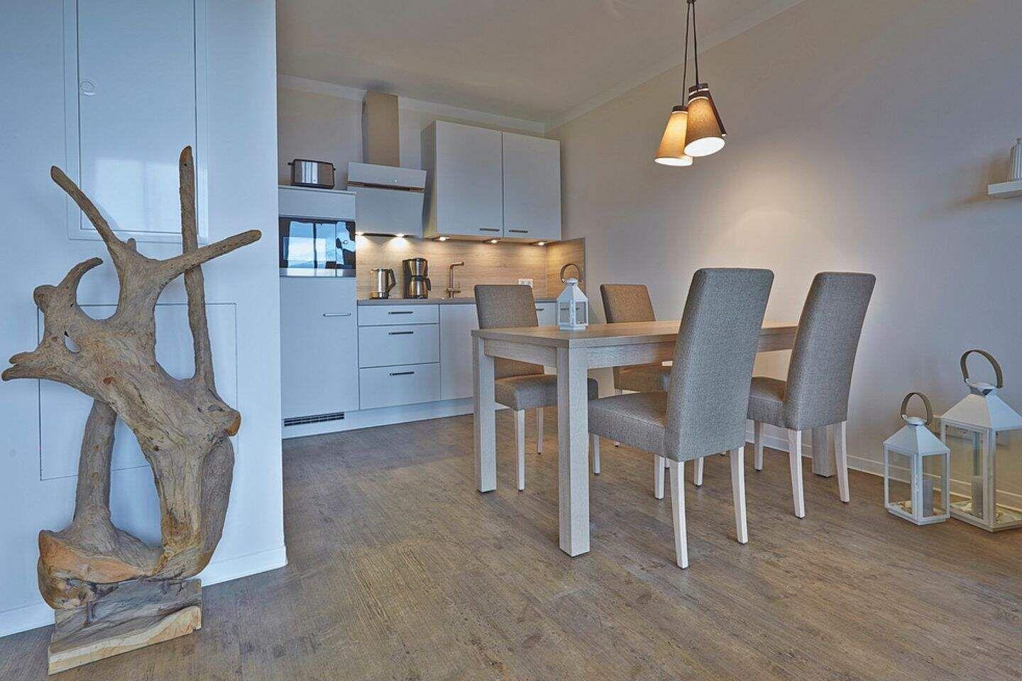 Essbereich mit Tisch und Stühlen, Küchenbereich im Hintergrund, Bodenbelag aus Holz, dekoratives Holzobjekt