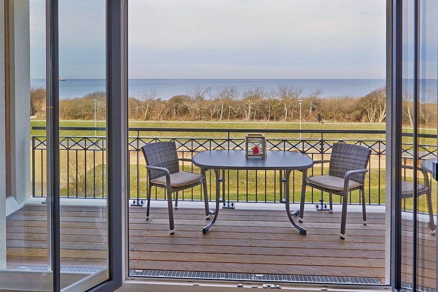 Terrasse mit Tisch und zwei Stühlen, Blick auf Meer und Grünfläche.