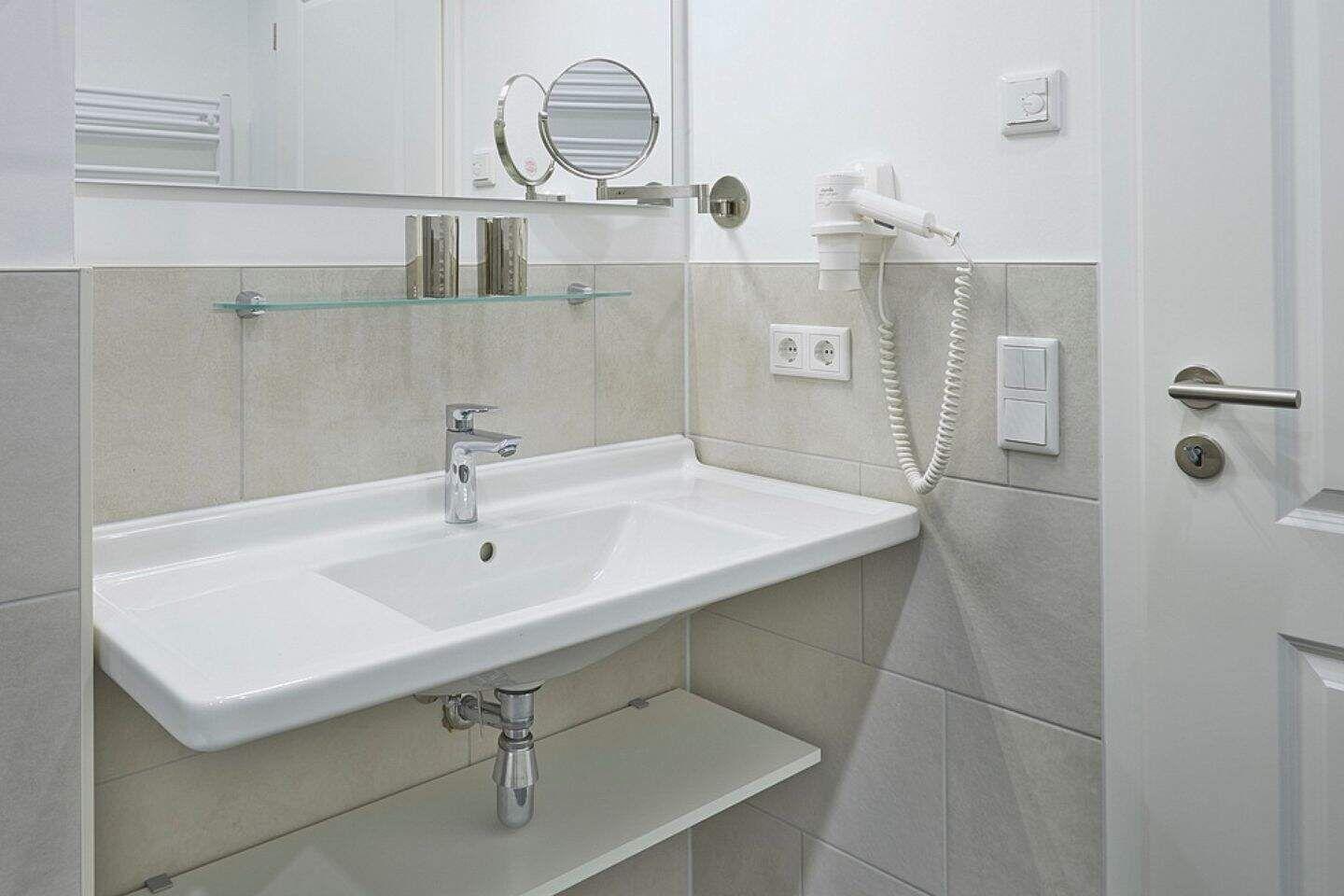 Badezimmer mit Waschbecken, Spiegel und Handtuchhalter.