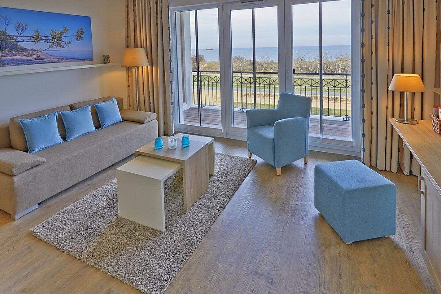 Wohnzimmer mit Sofa, Sessel und Balkonblick aufs Meer