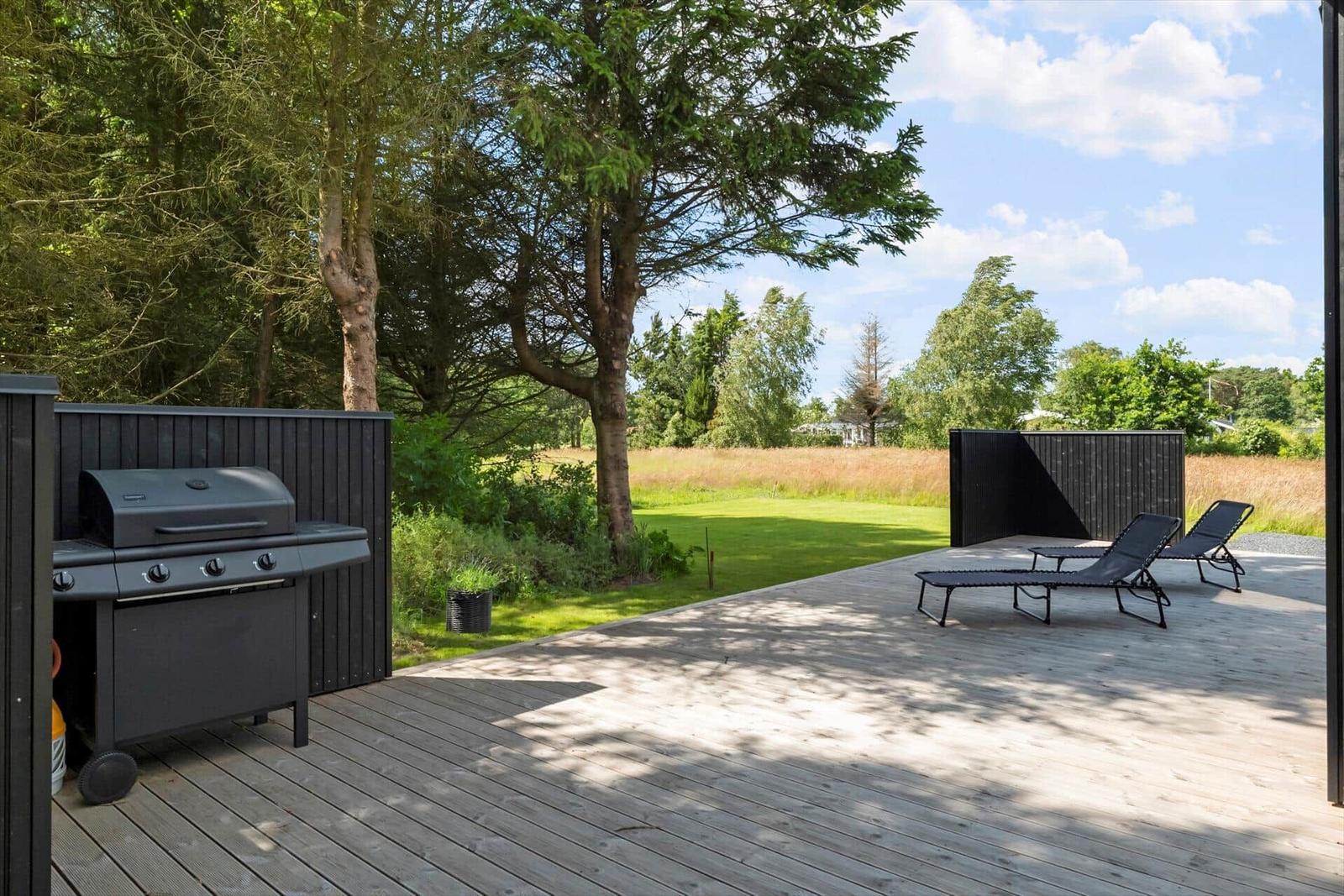 Terrasse mit Grill und Liegestühlen, umgeben von Grün und Bäumen.
