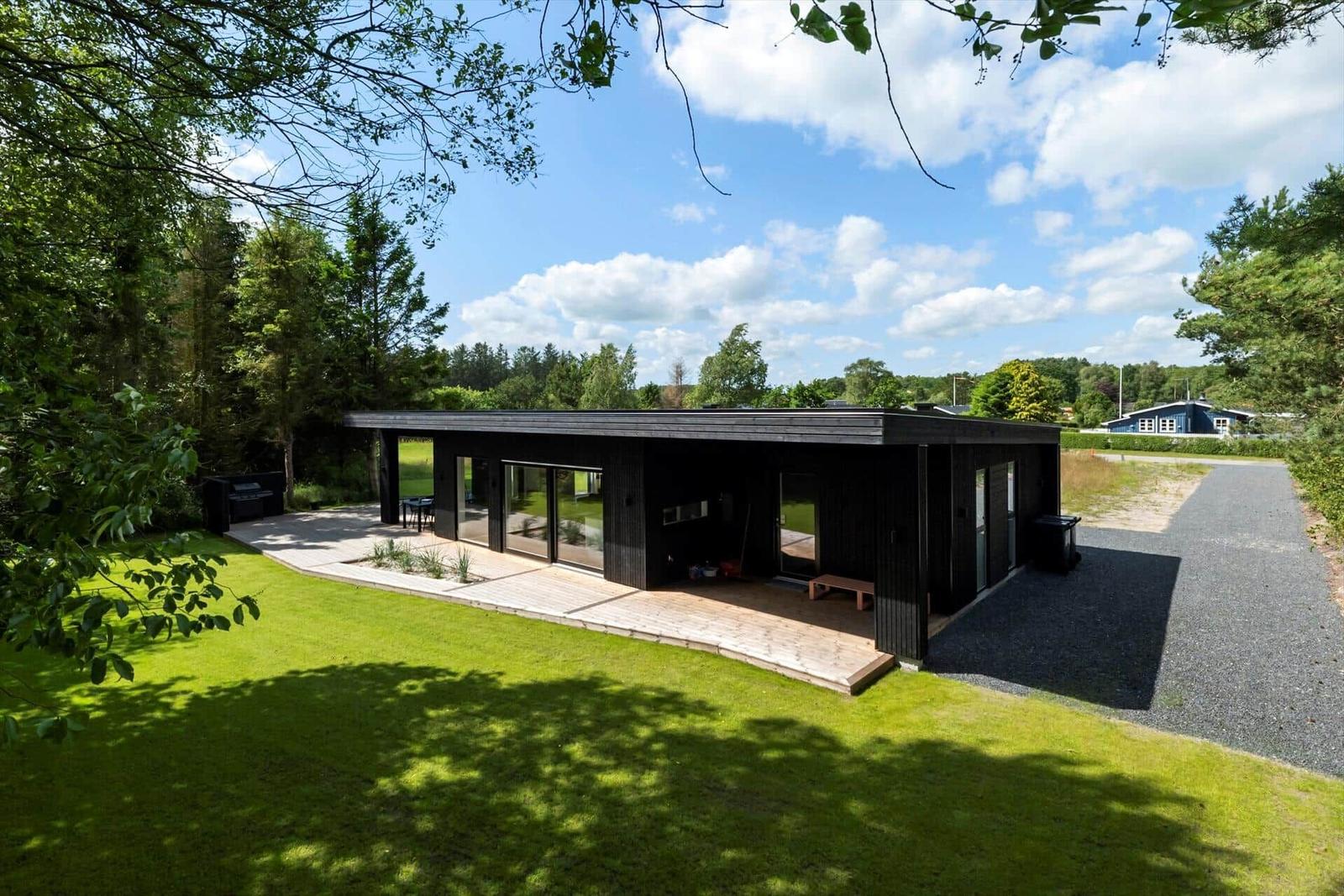 Moderne schwarze Hütte mit großem Glasbereich und Terrasse im Grünen.