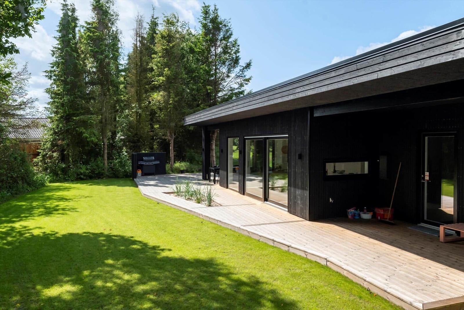 Moderne Villa mit Holzterrasse, Grünfläche und Grillbereich im Freien.