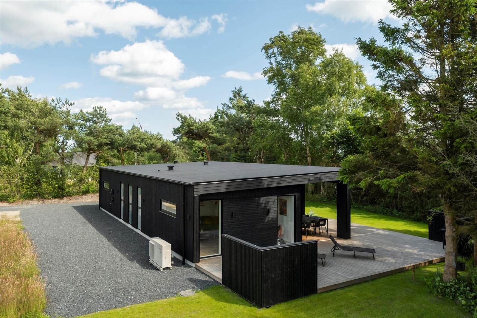 Moderne schwarze Villa mit Terrasse und Garten. Holzterrasse mit Liege und Tisch.