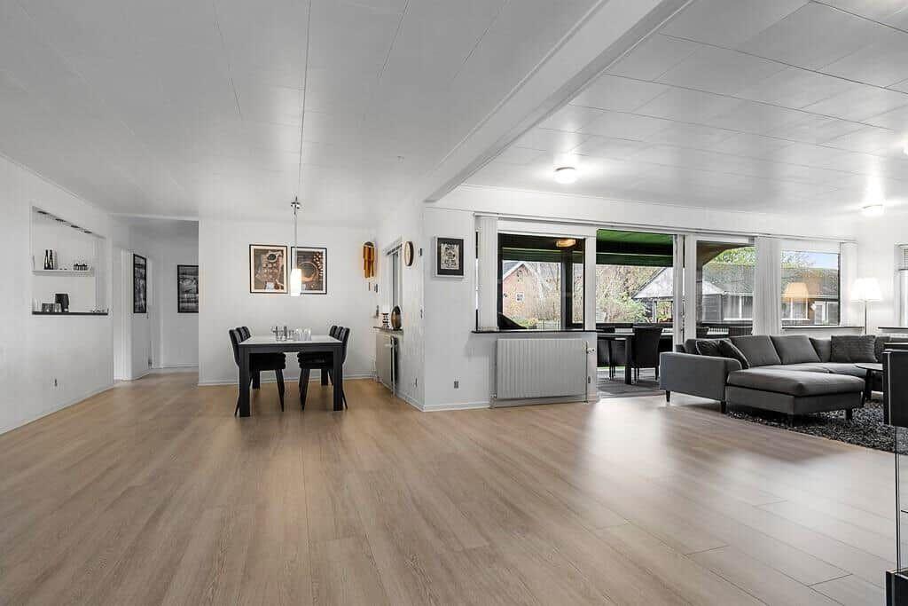 Wohn- und Essbereich mit Holzboden und großem Fenster. Sofa und Esstisch sind sichtbar.