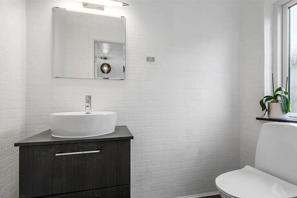 Badezimmer mit Waschbecken, Spiegel und Toilette. Fenster mit Pflanze.