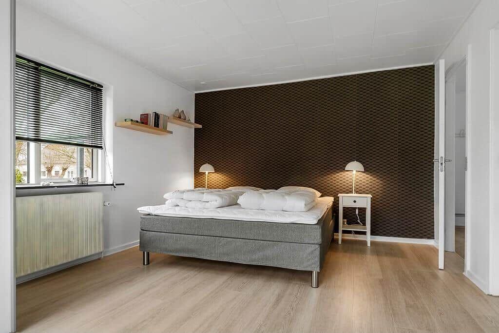 Schlafzimmer mit Bett, Nachttisch und Fenster. Wand mit strukturiertem Tapetenmuster.
