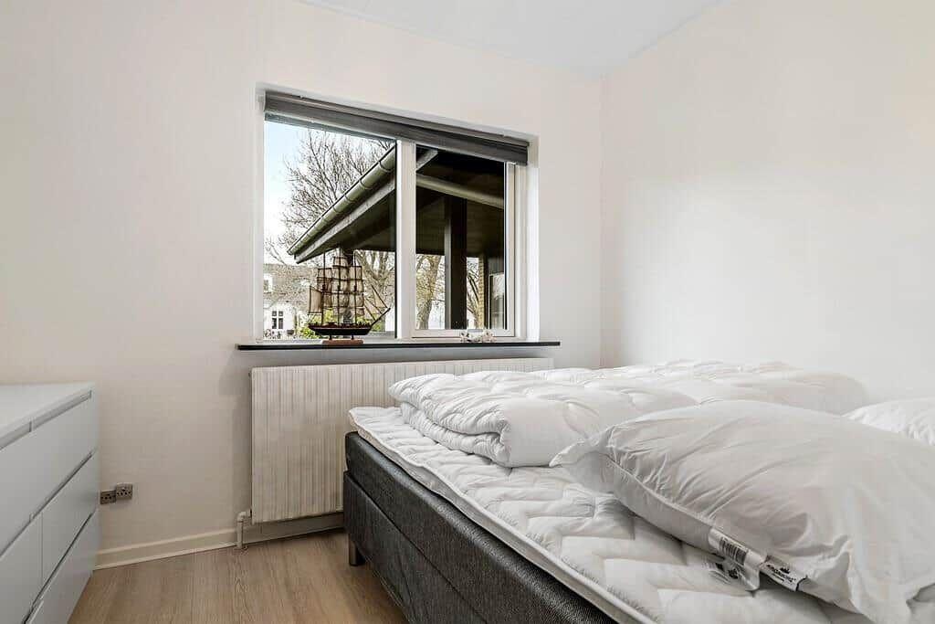 Schlafzimmer mit Bett, Fenster und Schrank. Auf dem Fensterbrett steht ein Schiffmodell.