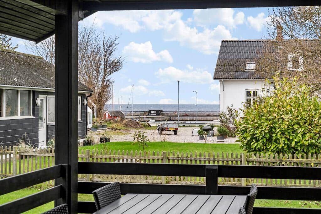 Terrasse mit Tisch und Stühlen bietet Blick auf Garten und See.