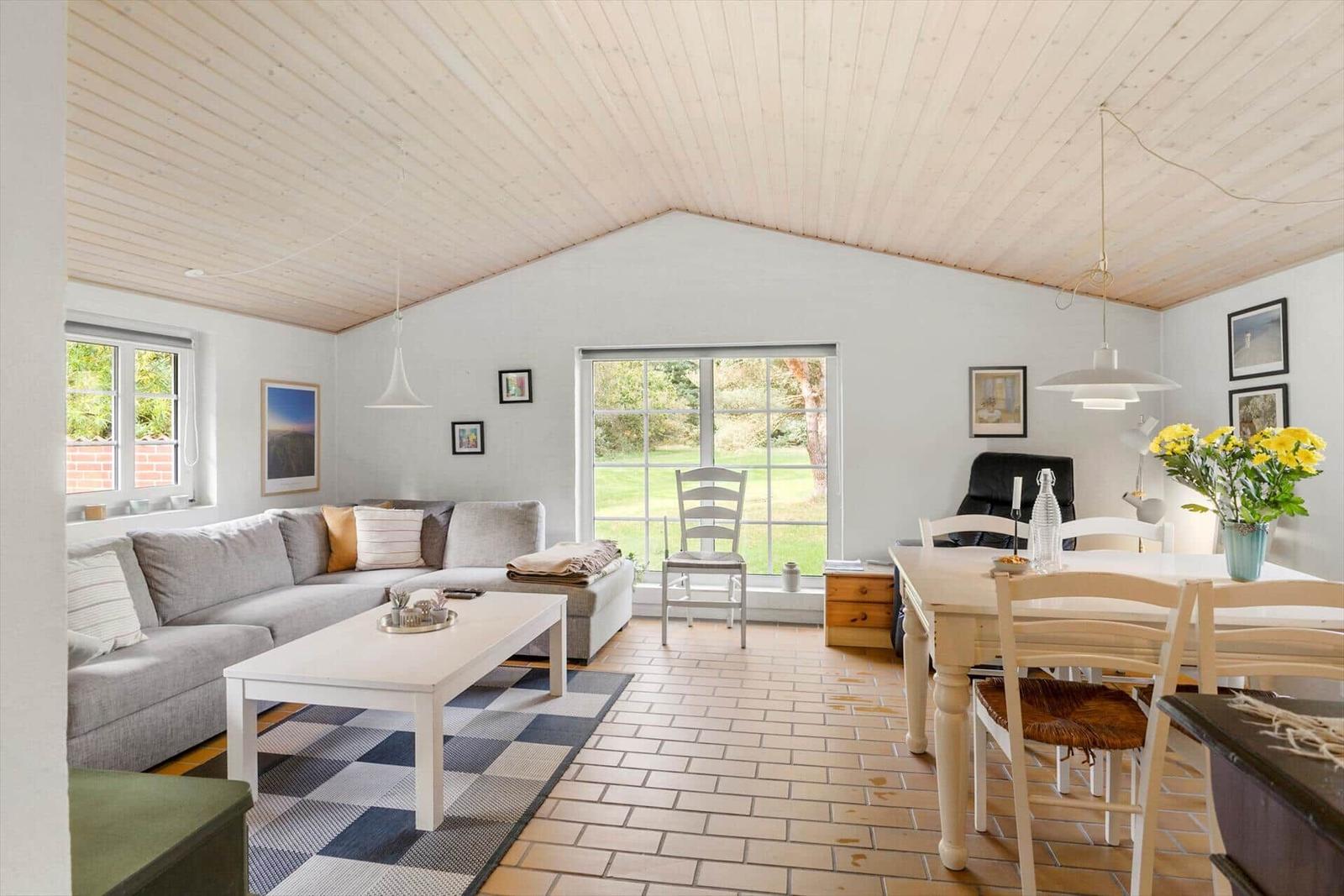 Wohn- und Essbereich mit Sofa, Tisch und Stühlen. Holzdecke und große Fenster.