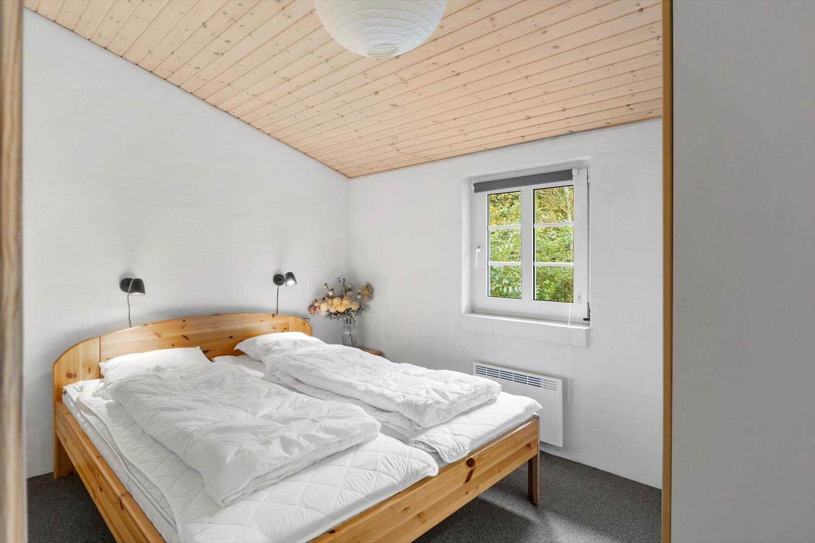 Ein Schlafzimmer mit Holzbett, Fenster und Decke.