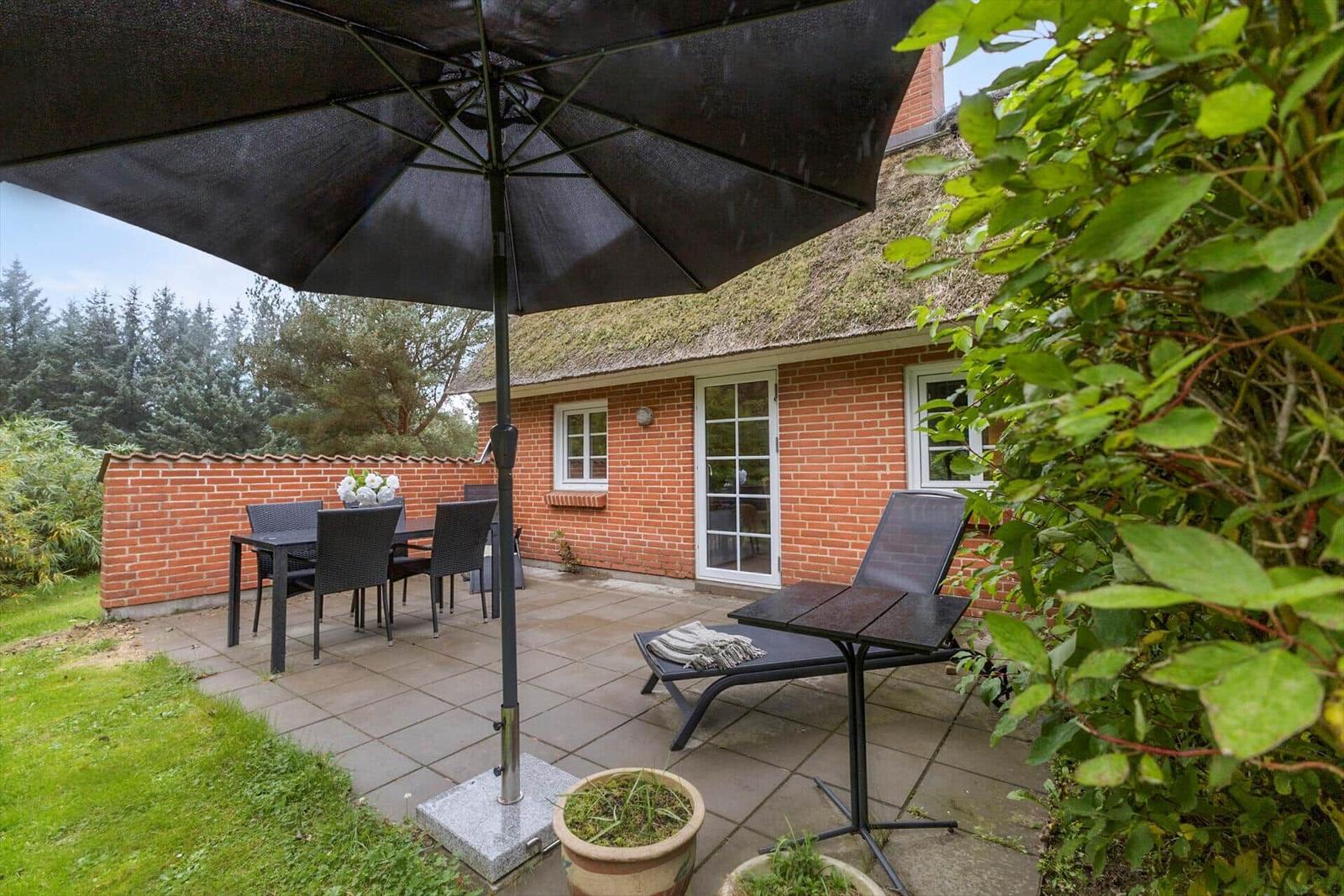 Terrasse mit Tisch, Stühlen und Sonnenschirm neben einem Haus mit rotem Ziegelmauerwerk.