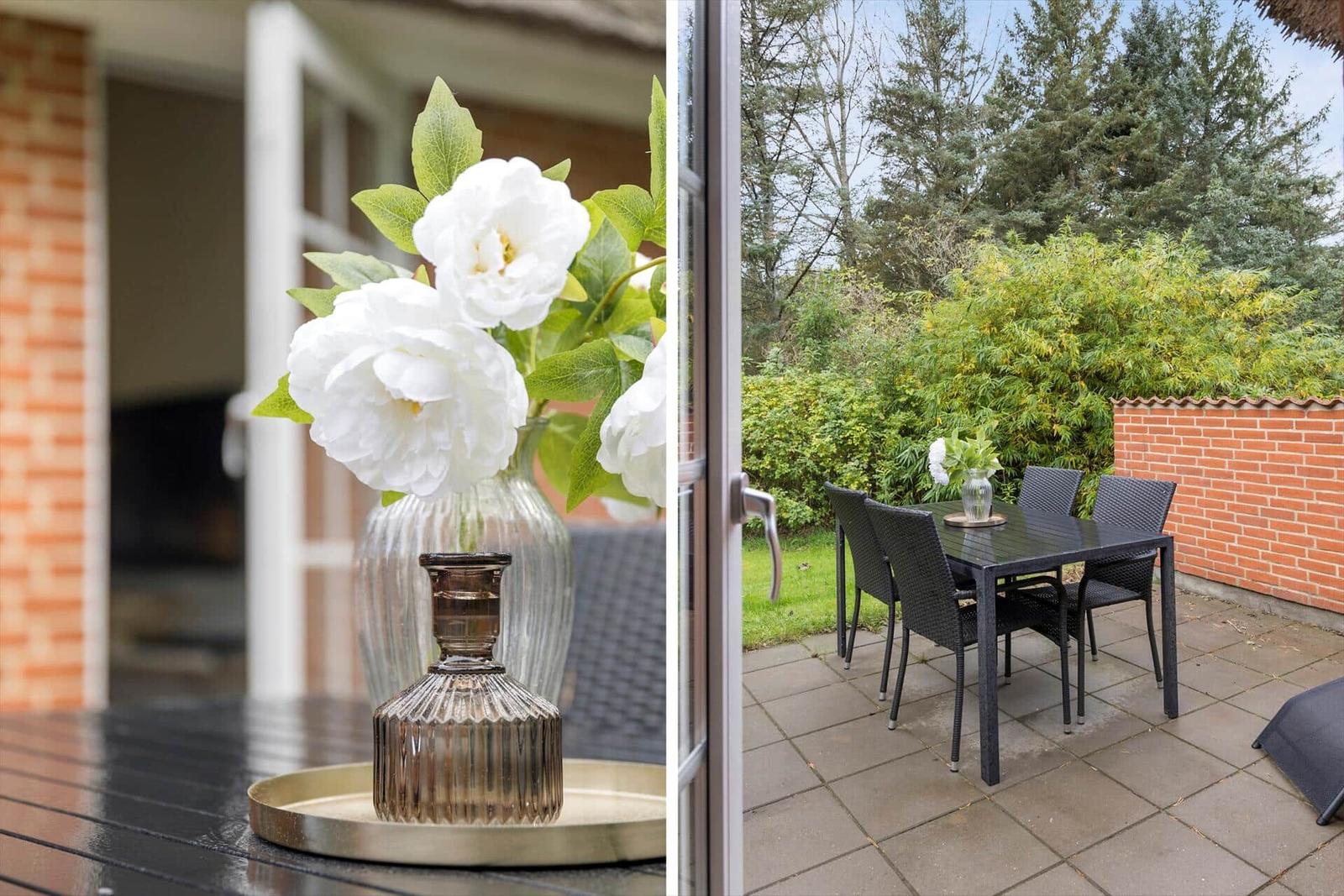 Terrasse mit Tisch und Stühlen, Blumenarrangement und Blick auf grüne Hecke.
