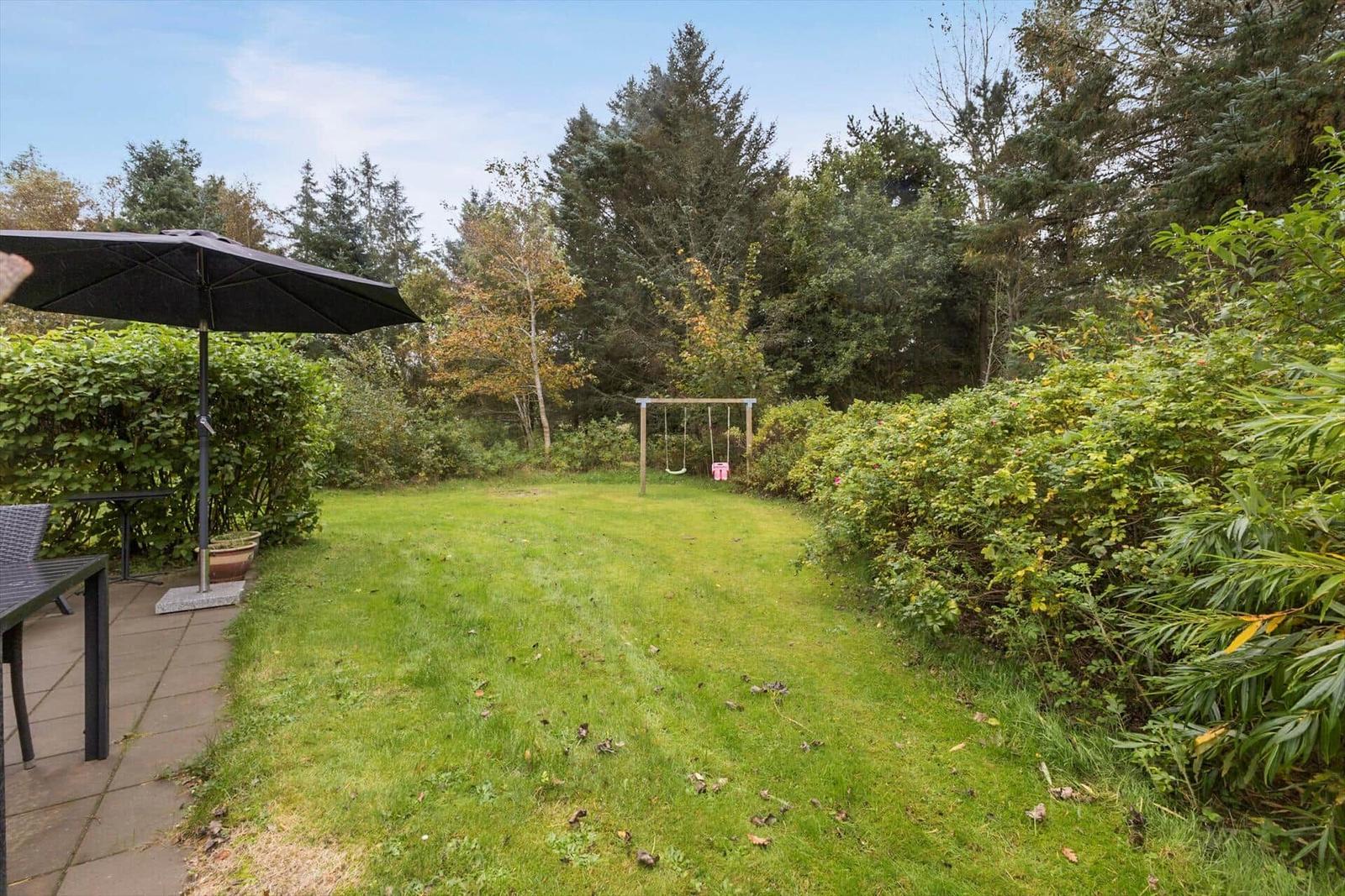 Hinterhof mit Grünfläche, Schaukel und Terrasse mit Sonnenschirm.