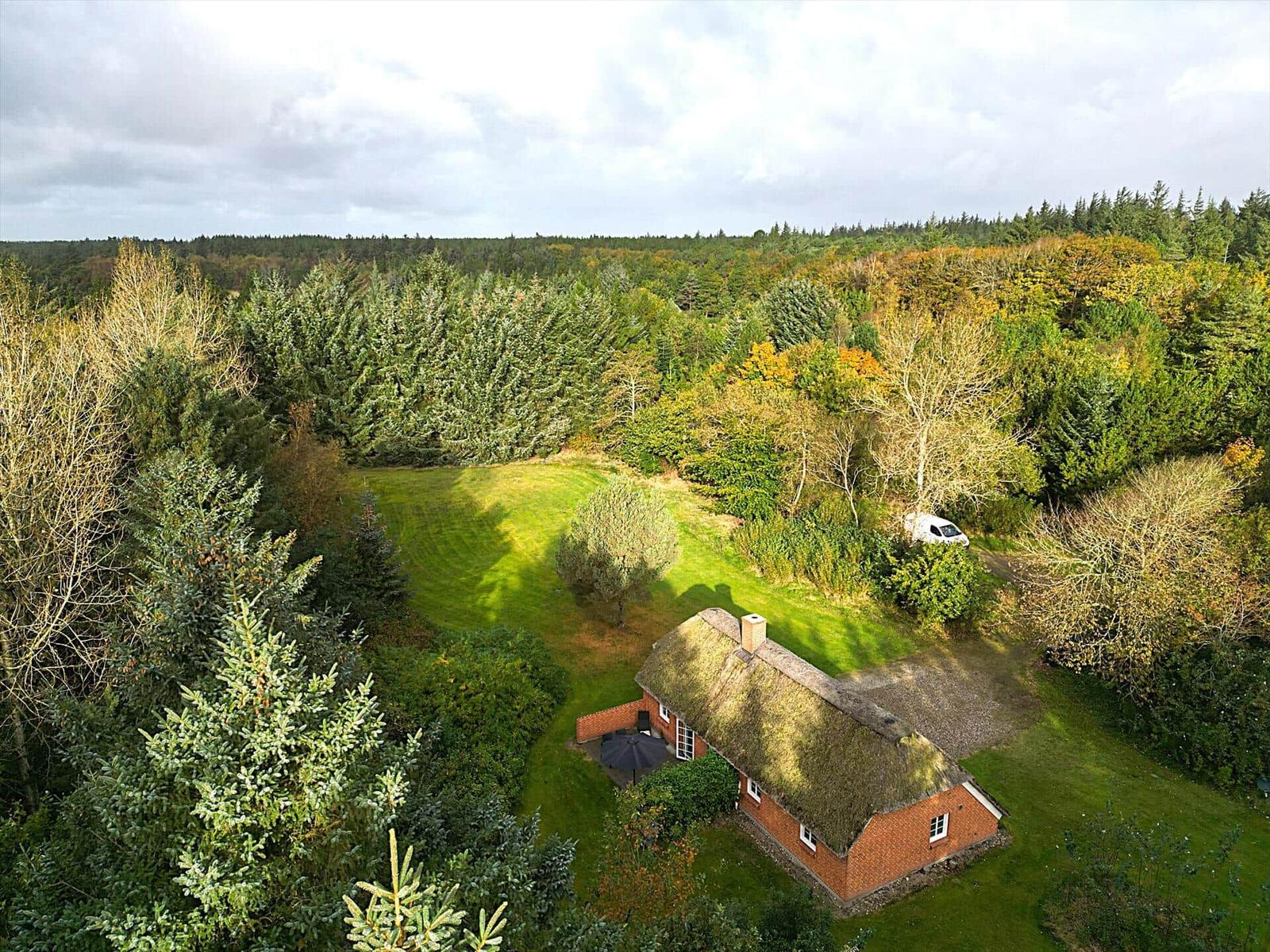 Haus mit Strohdach und Garten umgeben von Wald und Bäumen.