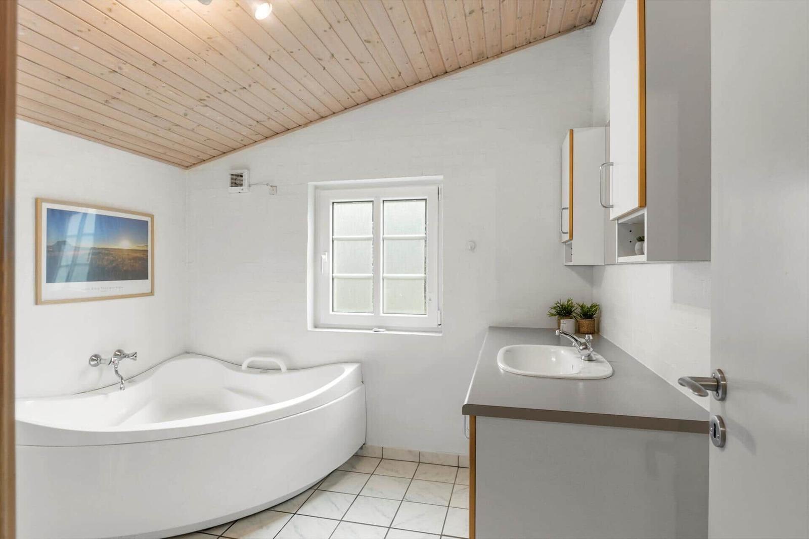 Badezimmer mit Badewanne, Waschbecken und Fenster.