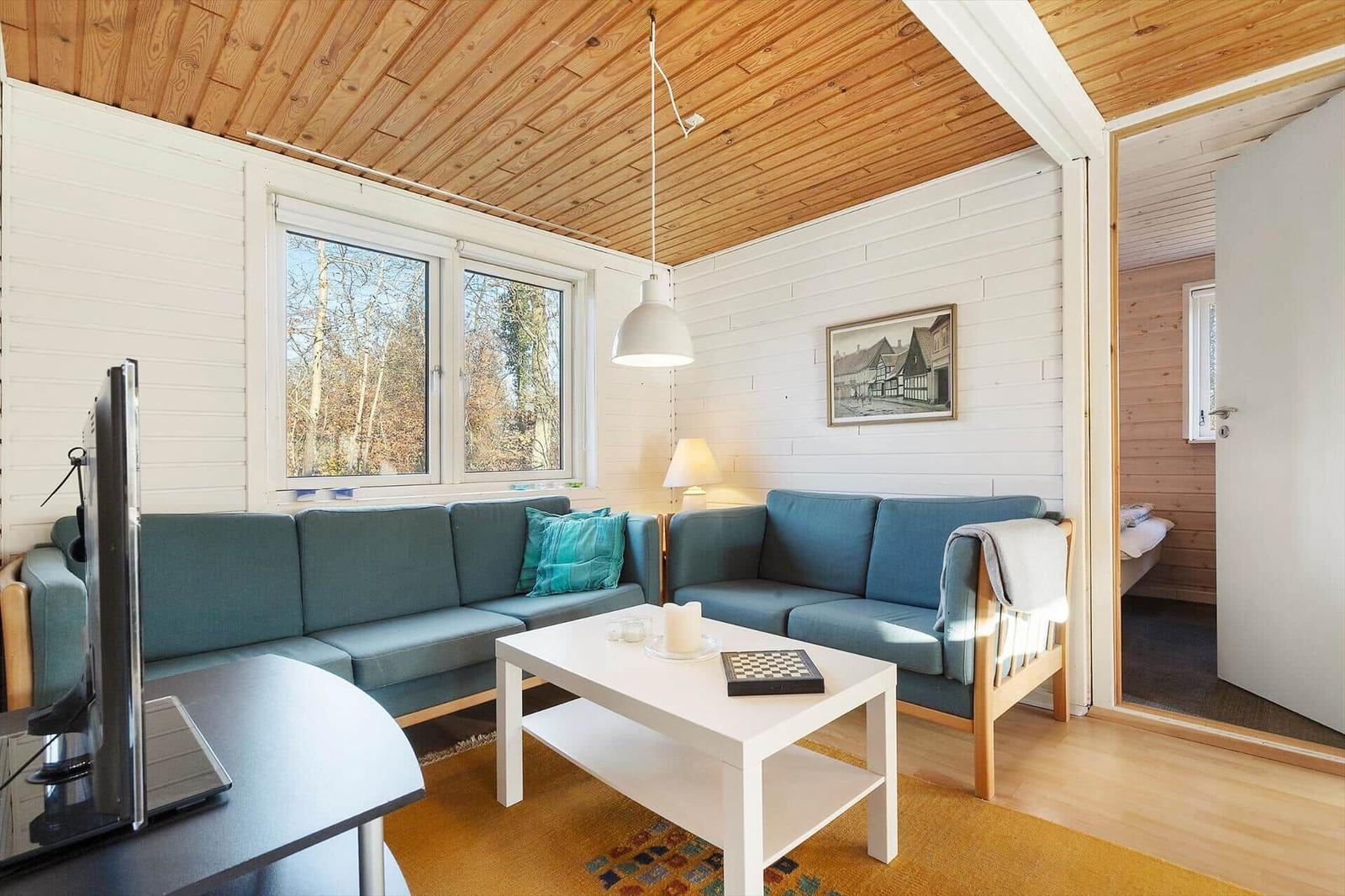Living room with blue sofa, white table, and wooden ceiling. View of forest through windows.