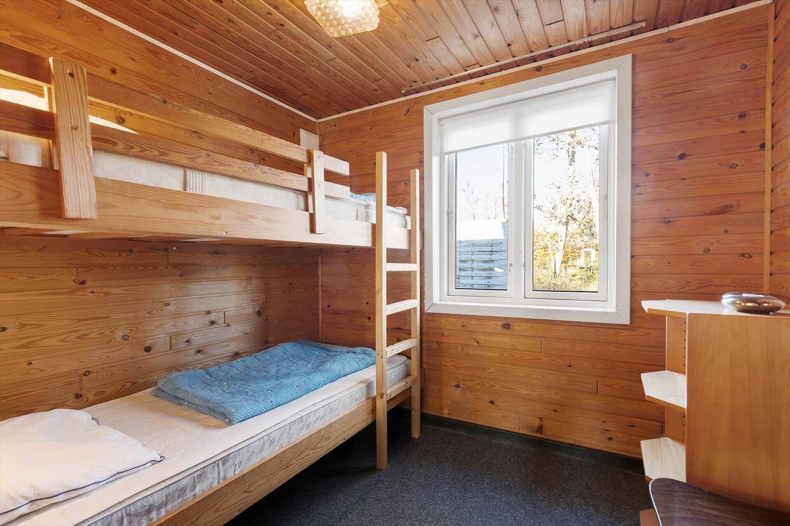 Room with bunk bed, wooden walls, and window with view outside.