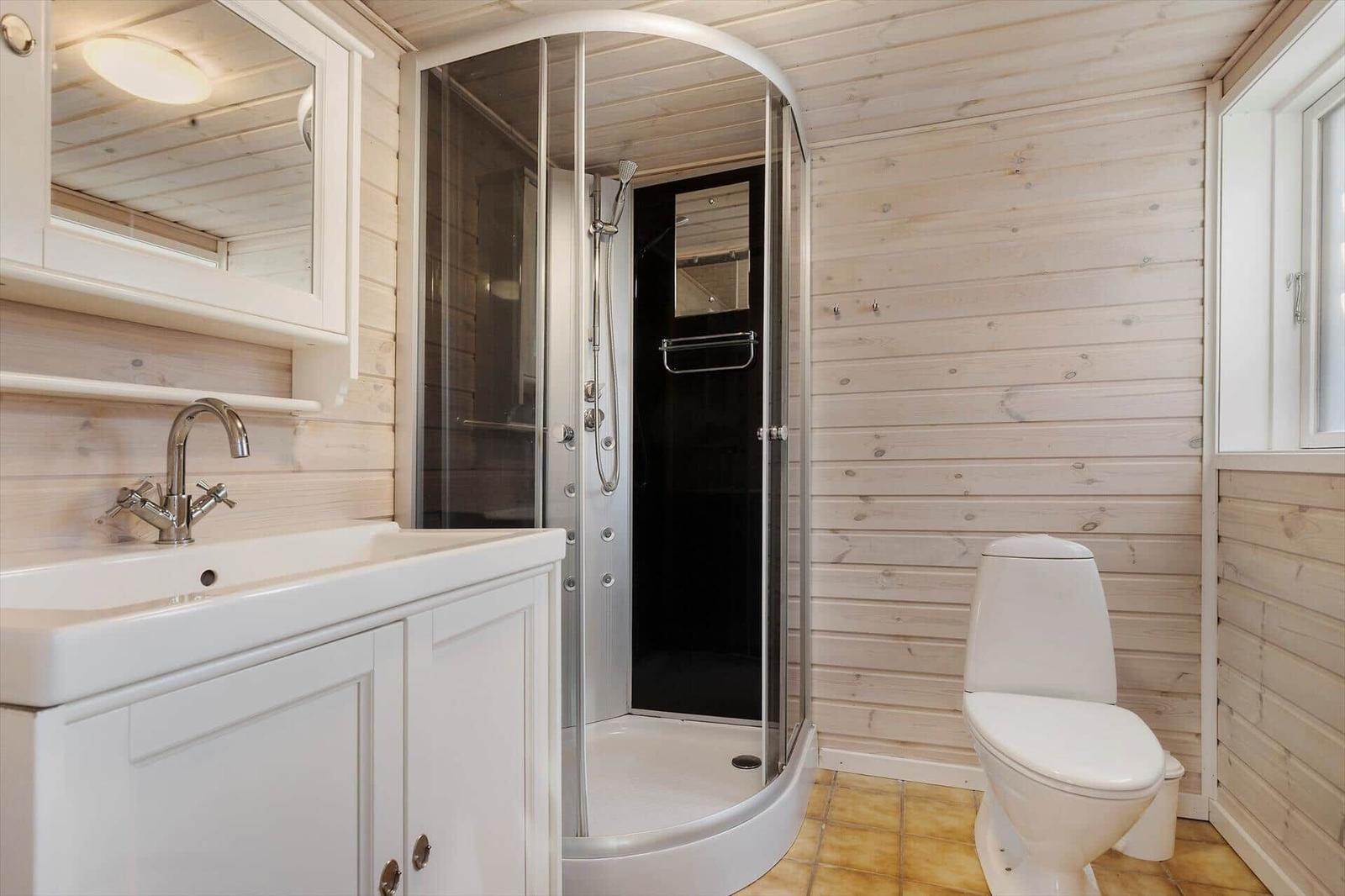 Bathroom with shower, sink and toilet against wooden wall