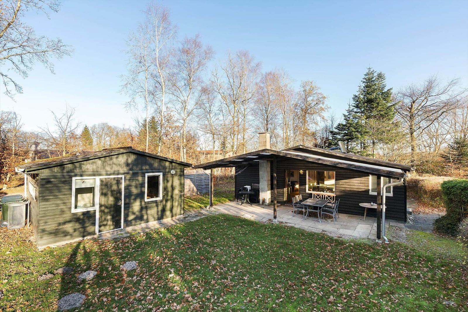 House with terrace, garden, and trees in the background.