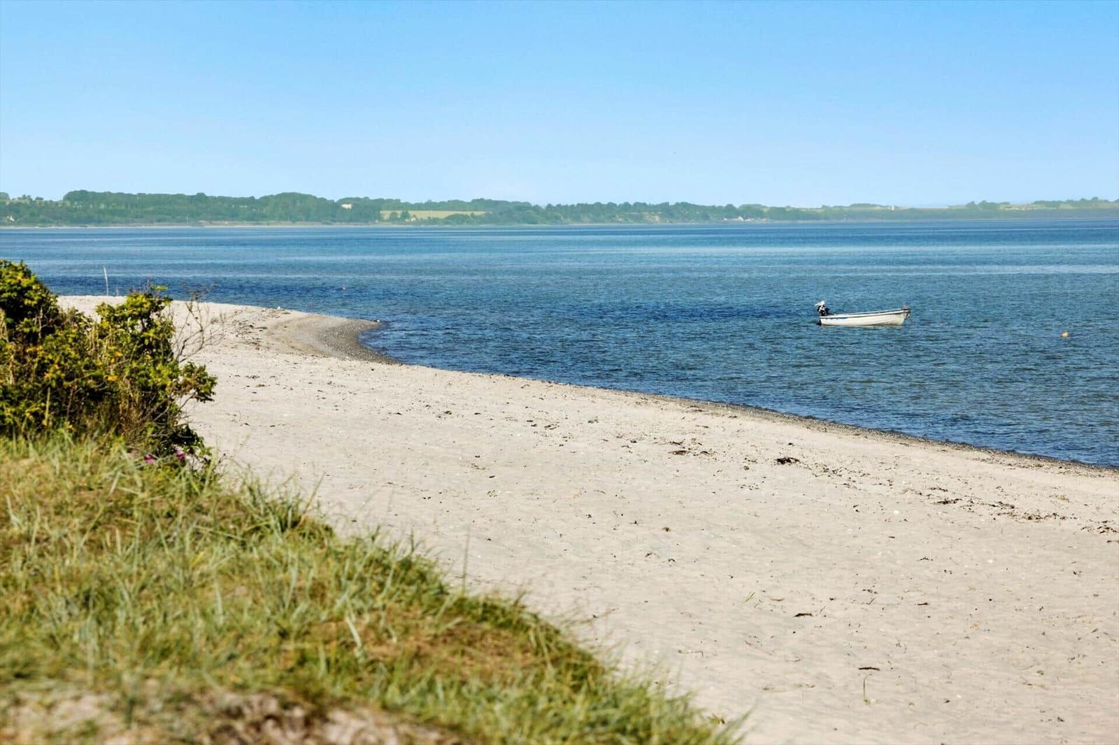 Beach with a white boat in the water and green vegetation along the shore.