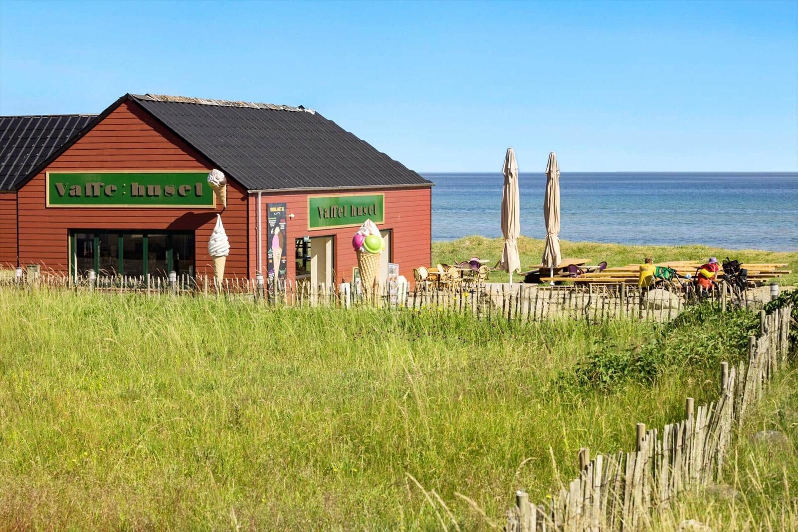 Red building with ice cream stands by the beach. Outdoor terrace with tables and umbrellas.