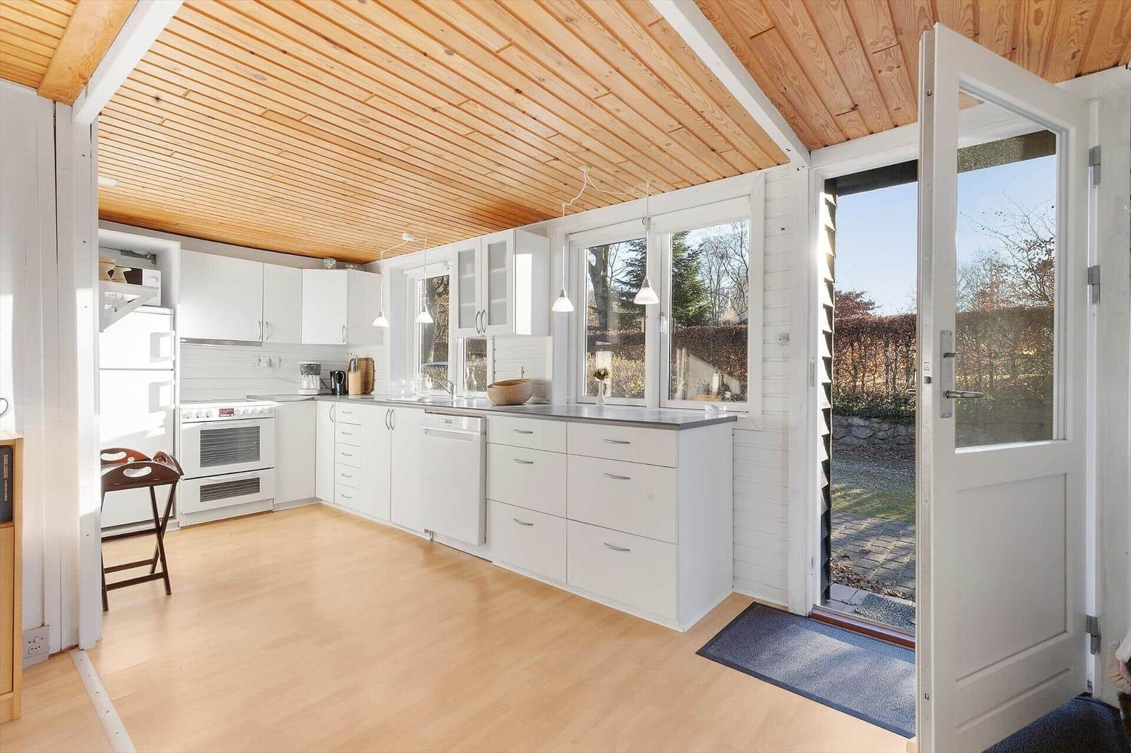 Kitchen with white cabinets, wooden floor, and roof. Door leads outside.