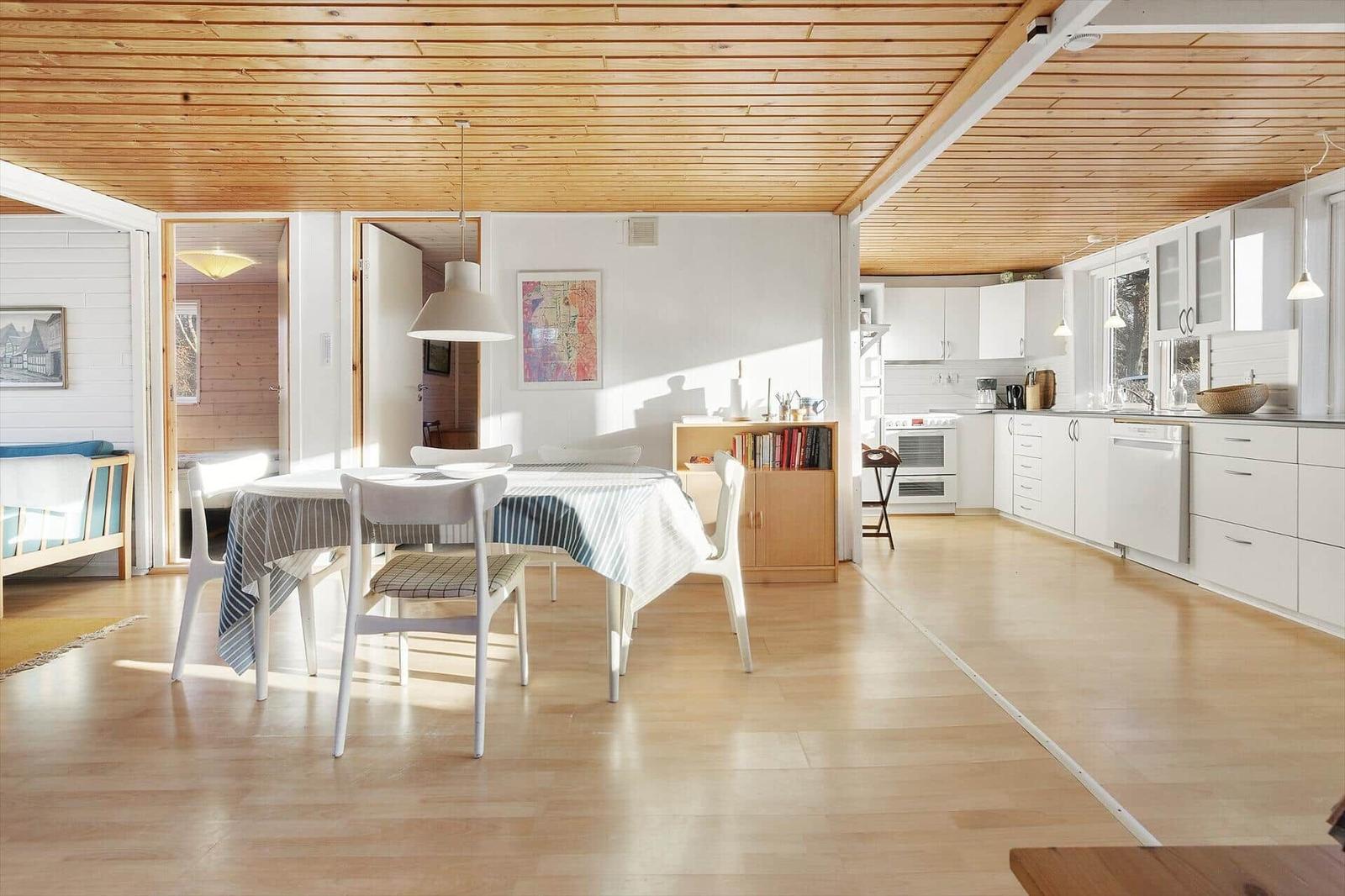 Living kitchen with dining table, white chairs, and wooden ceiling.